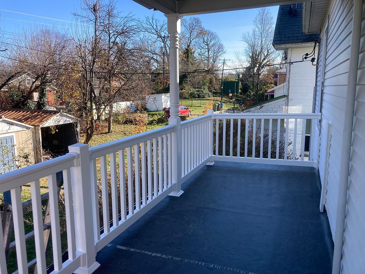 There is a porch with a white railing and a view of the backyard.