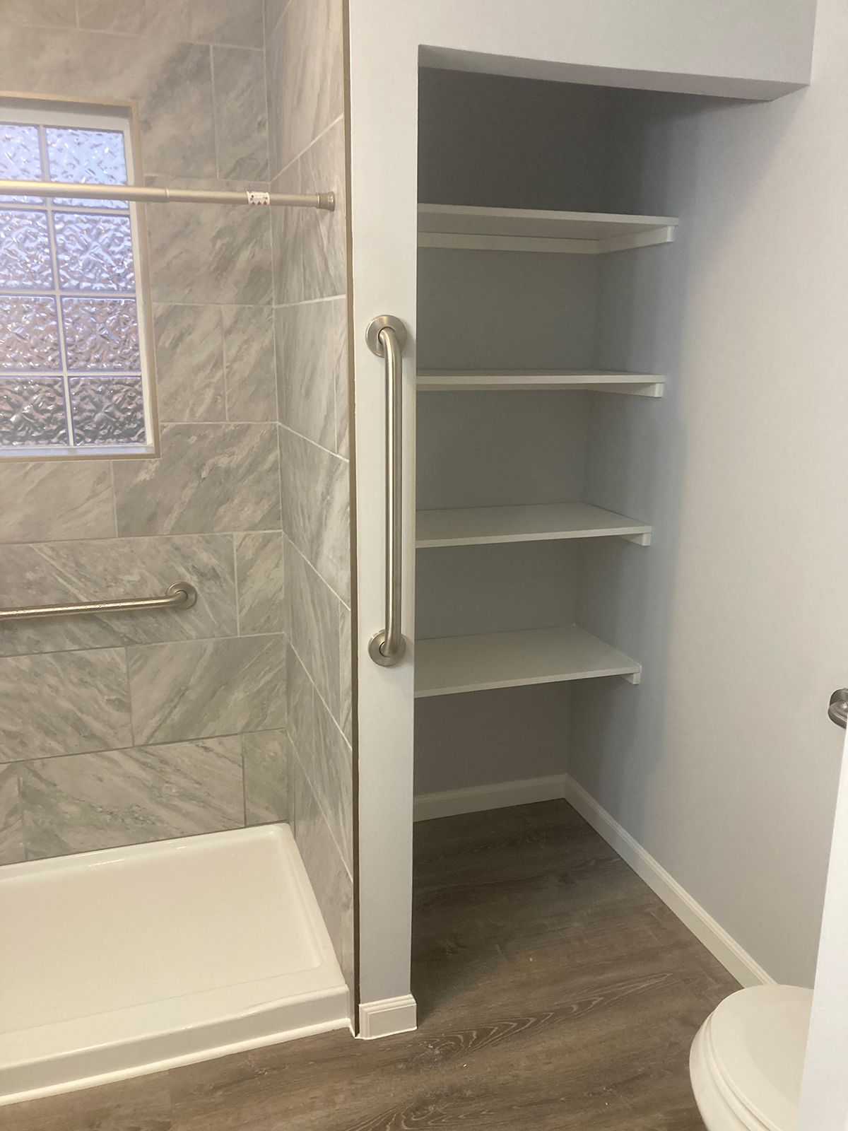 A bathroom with a walk in shower , toilet and shelves.