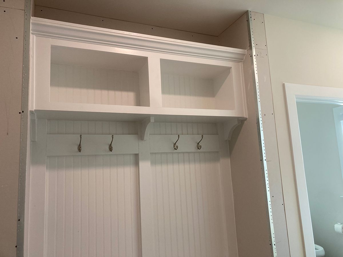 A white cabinet with hooks and shelves in a hallway