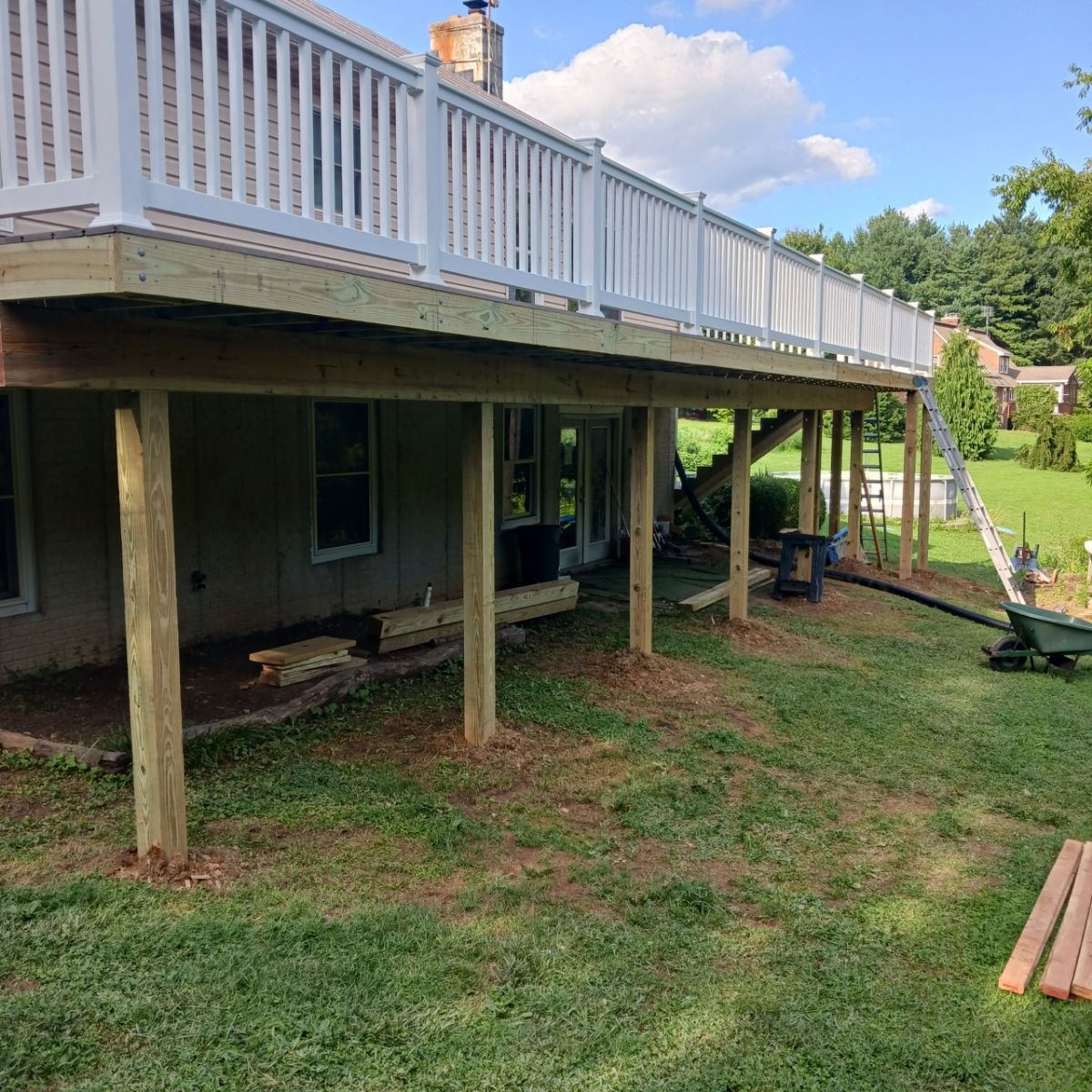 A wooden deck with a white railing is being built under a house.