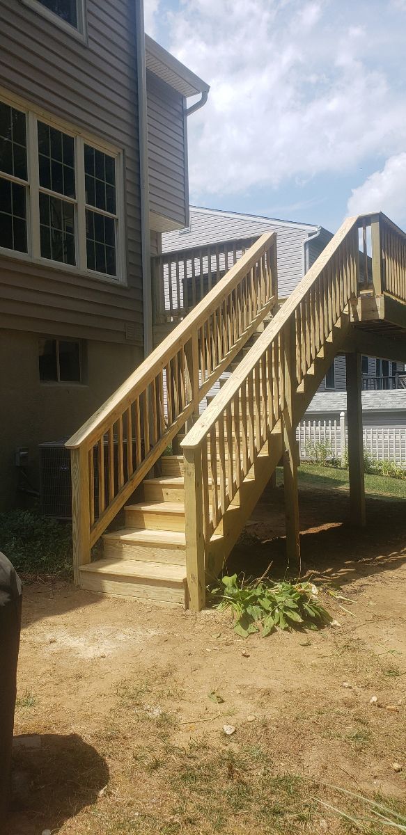 A wooden deck with stairs leading up to it and a house in the background.