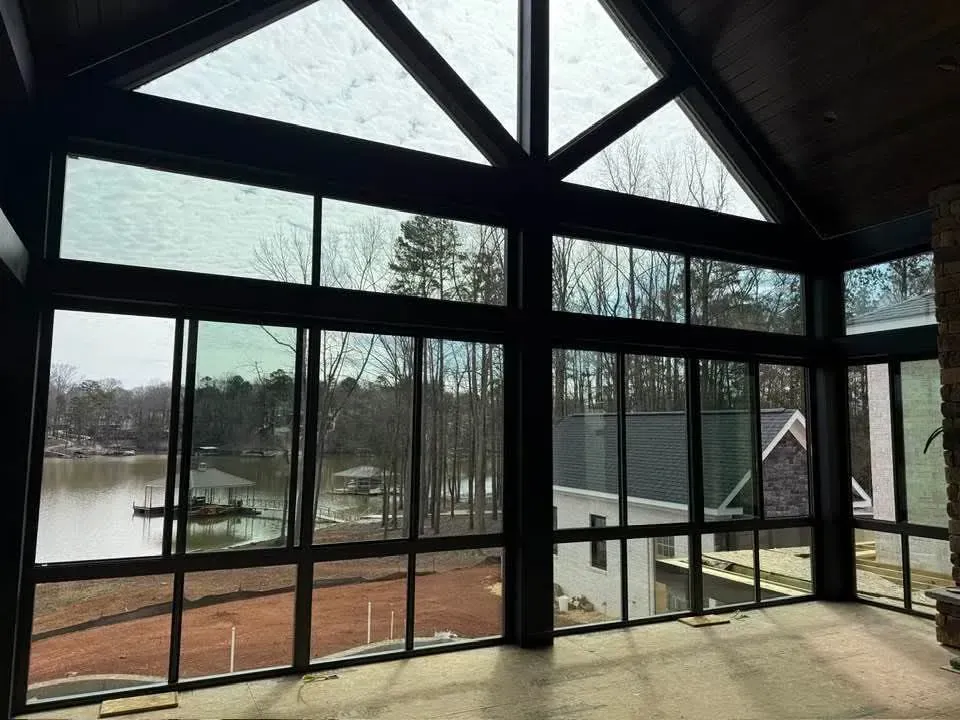 Sunroom with large windows overlooking a lake and trees, showing dark wood beams and a brick floor.