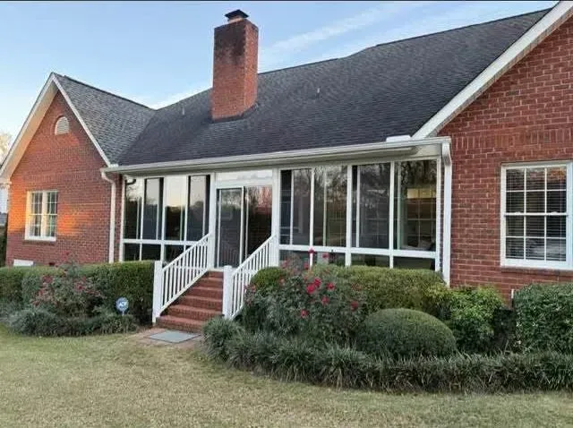 Brick house with a screened porch, white railings, and shrubs in front