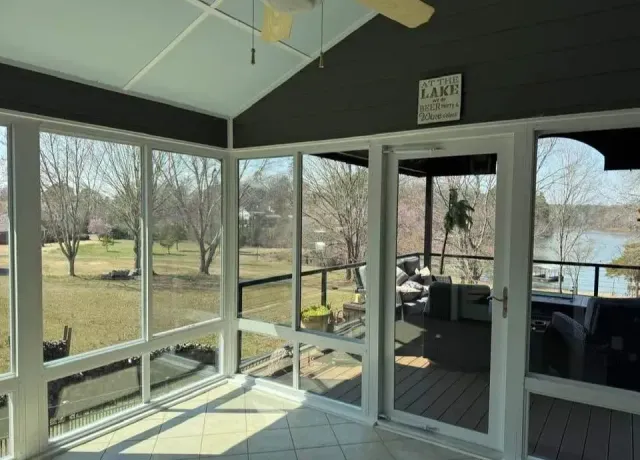 Sunroom with large windows overlooking a lawn and pond, white framing, and screened porch seating area