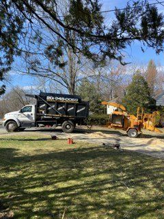 a dump truck is parked in a driveway next to a tree chipper .