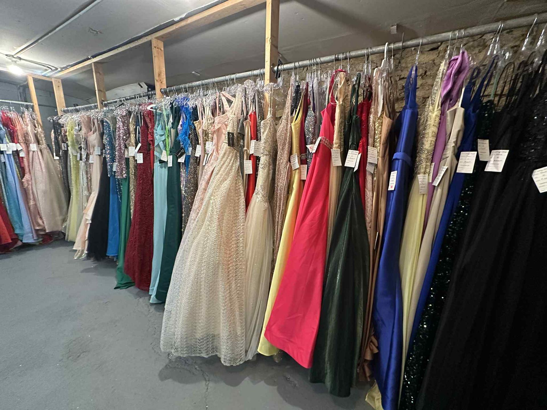 Row of colorful formal dresses hanging on racks in a retail store.