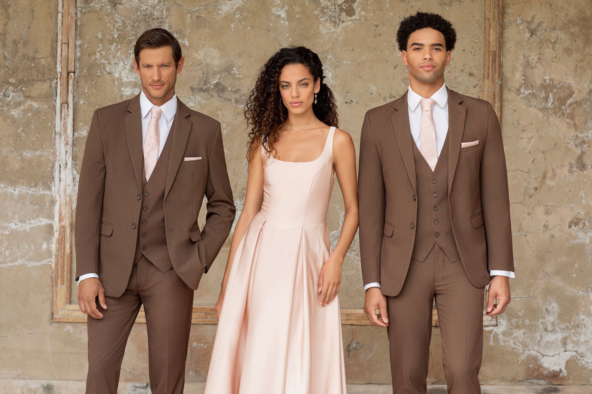 Three people in formal wear; woman in a blush dress, men in brown suits with blush ties.