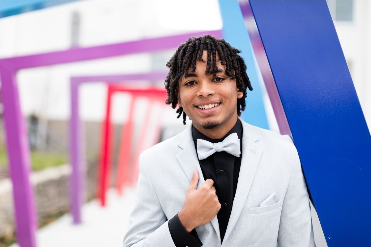 Man in light gray suit with bowtie, smiling, posing by colorful geometric structure.