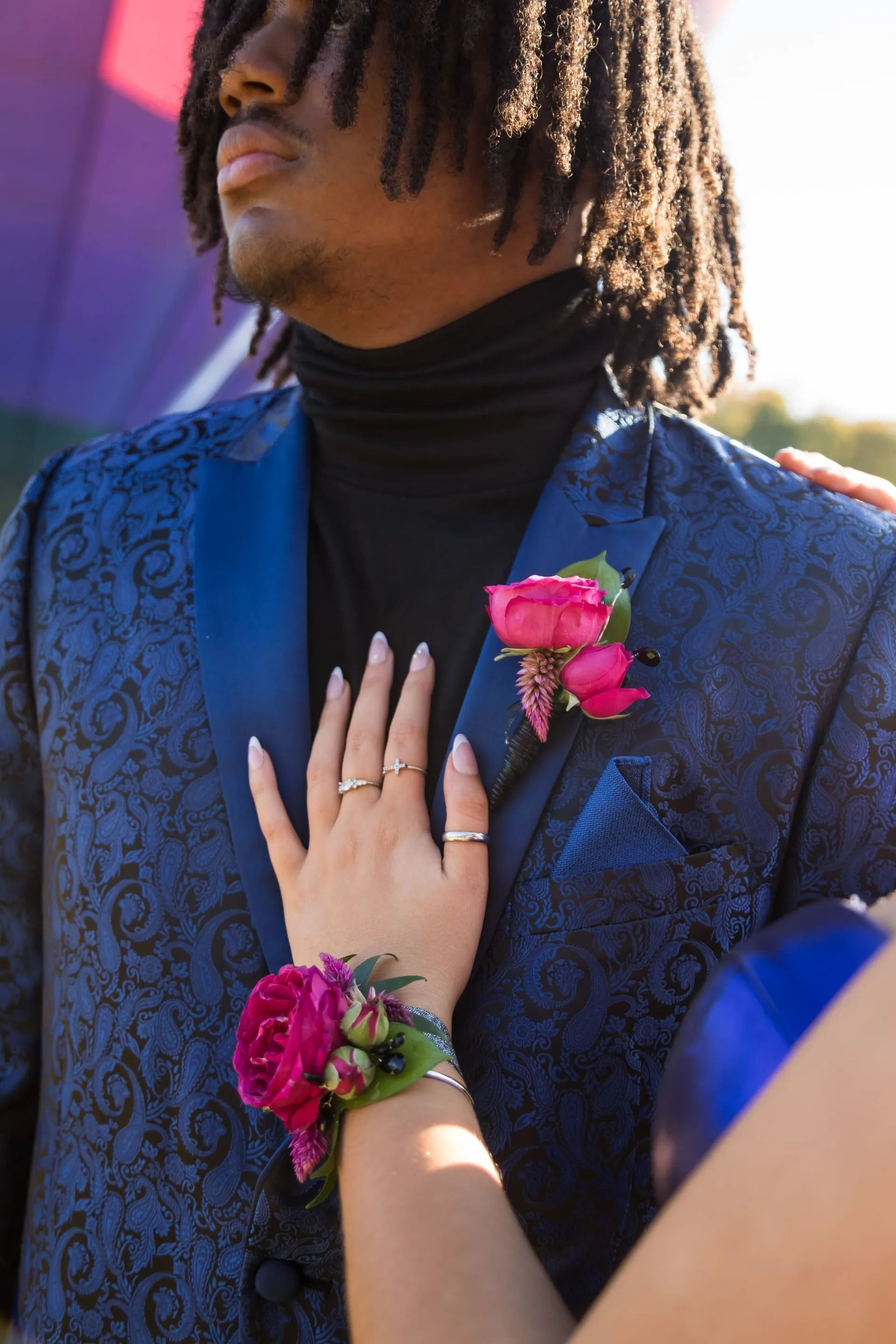 Person in blue patterned suit with a flower, hand on chest, hand with wrist corsage.