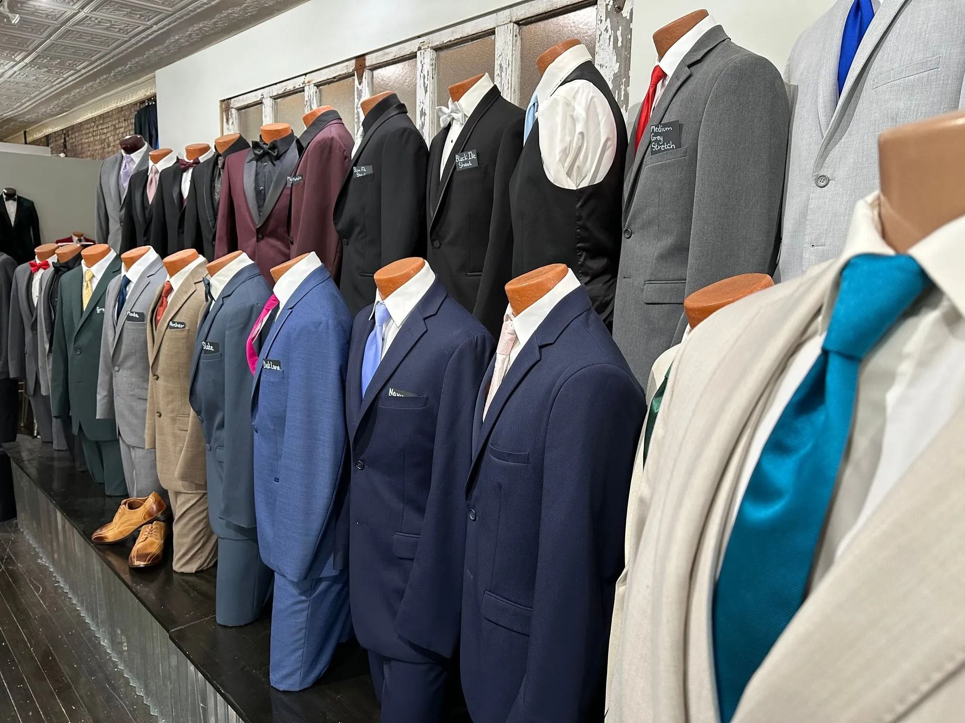 Mannequins wearing various suits in a clothing store display, different colors and styles.