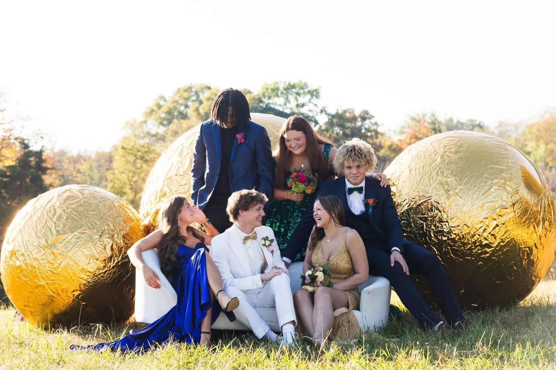 Group of teens in formal wear pose outdoors next to large golden spheres.