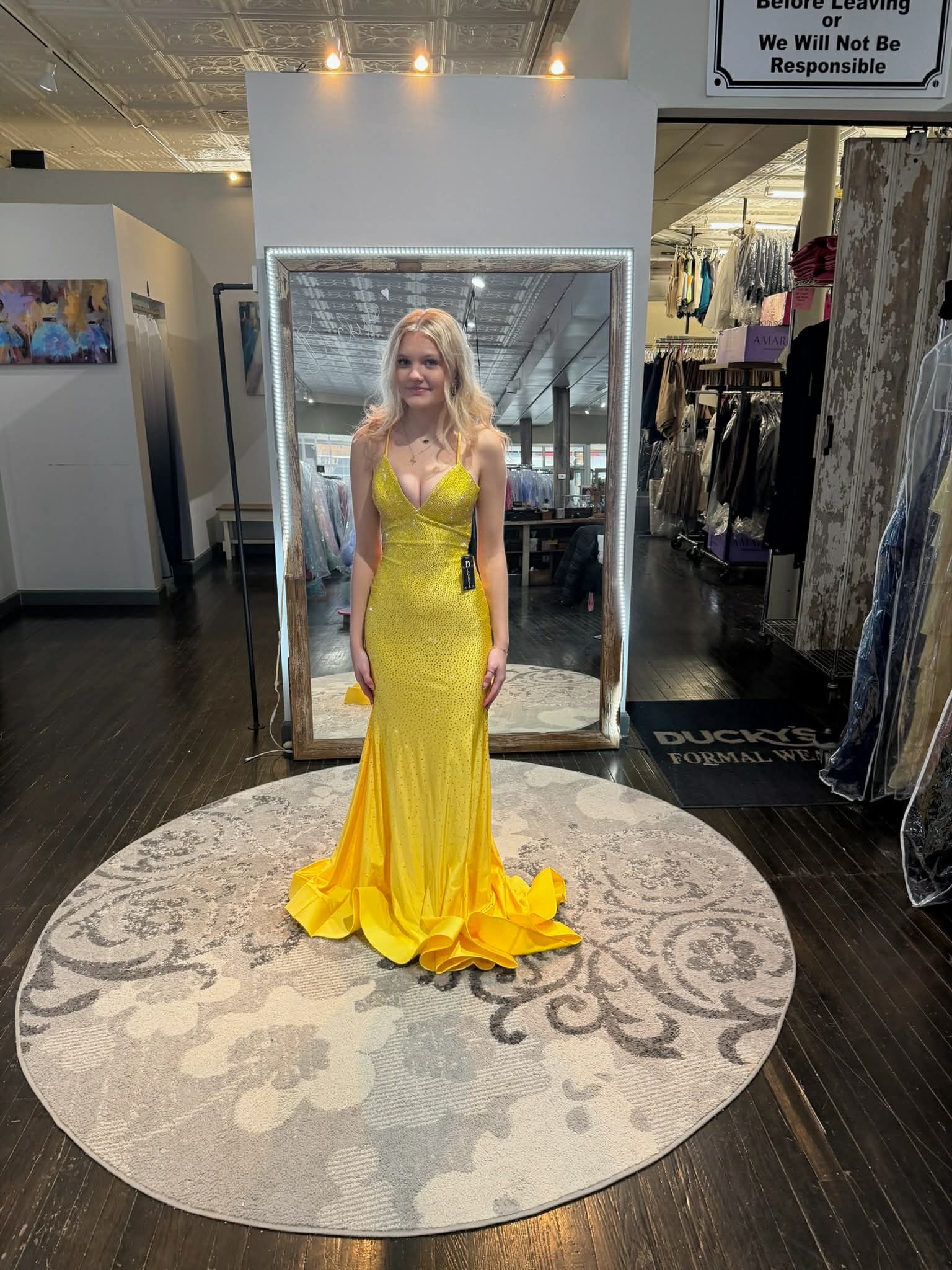 A person standing on a round rug in a clothing boutique, wearing a floor-length, bright yellow embellished gown.