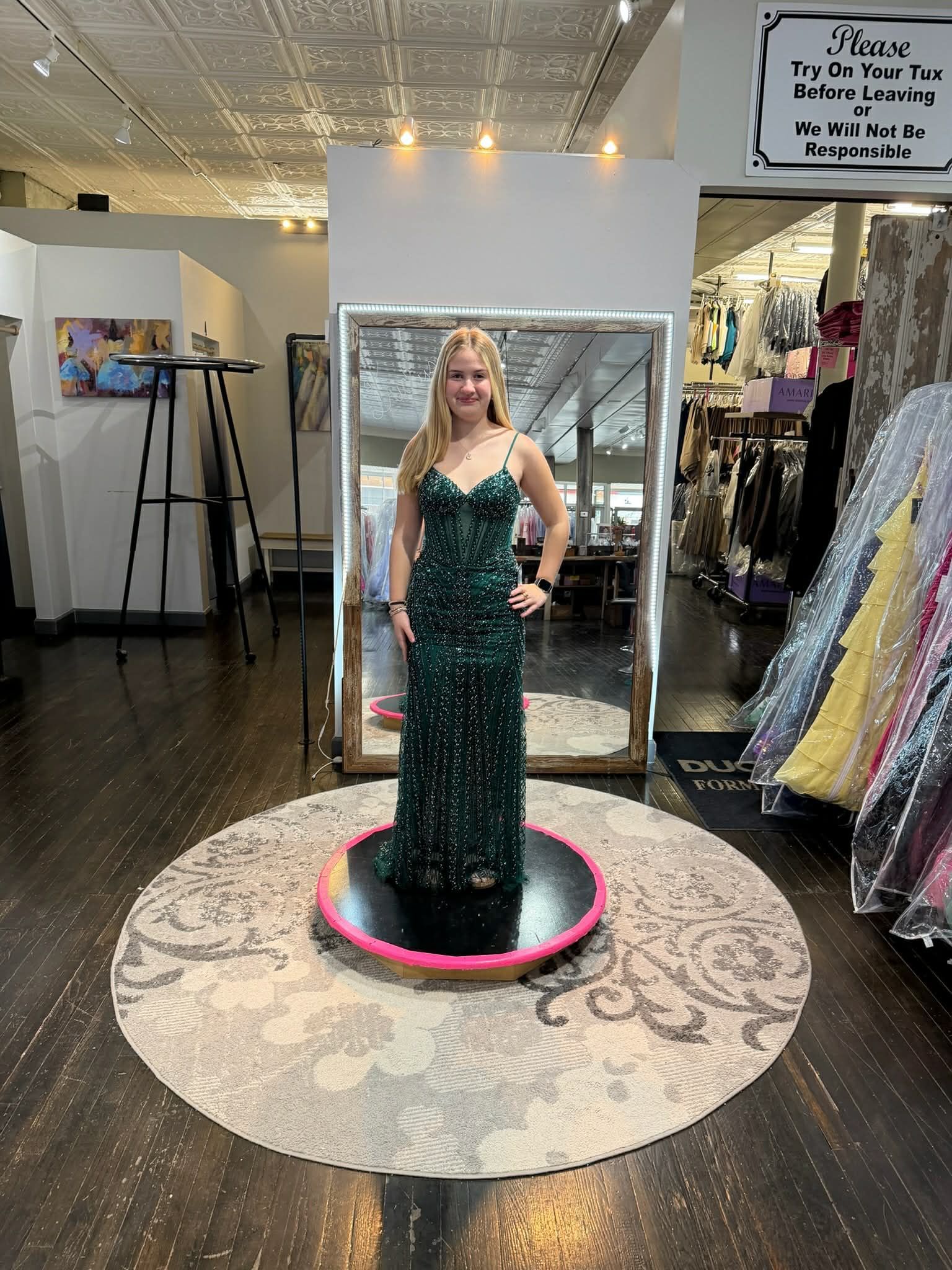 A person wearing a floor-length, dark green sequined gown stands on a circular platform in a bridal shop.