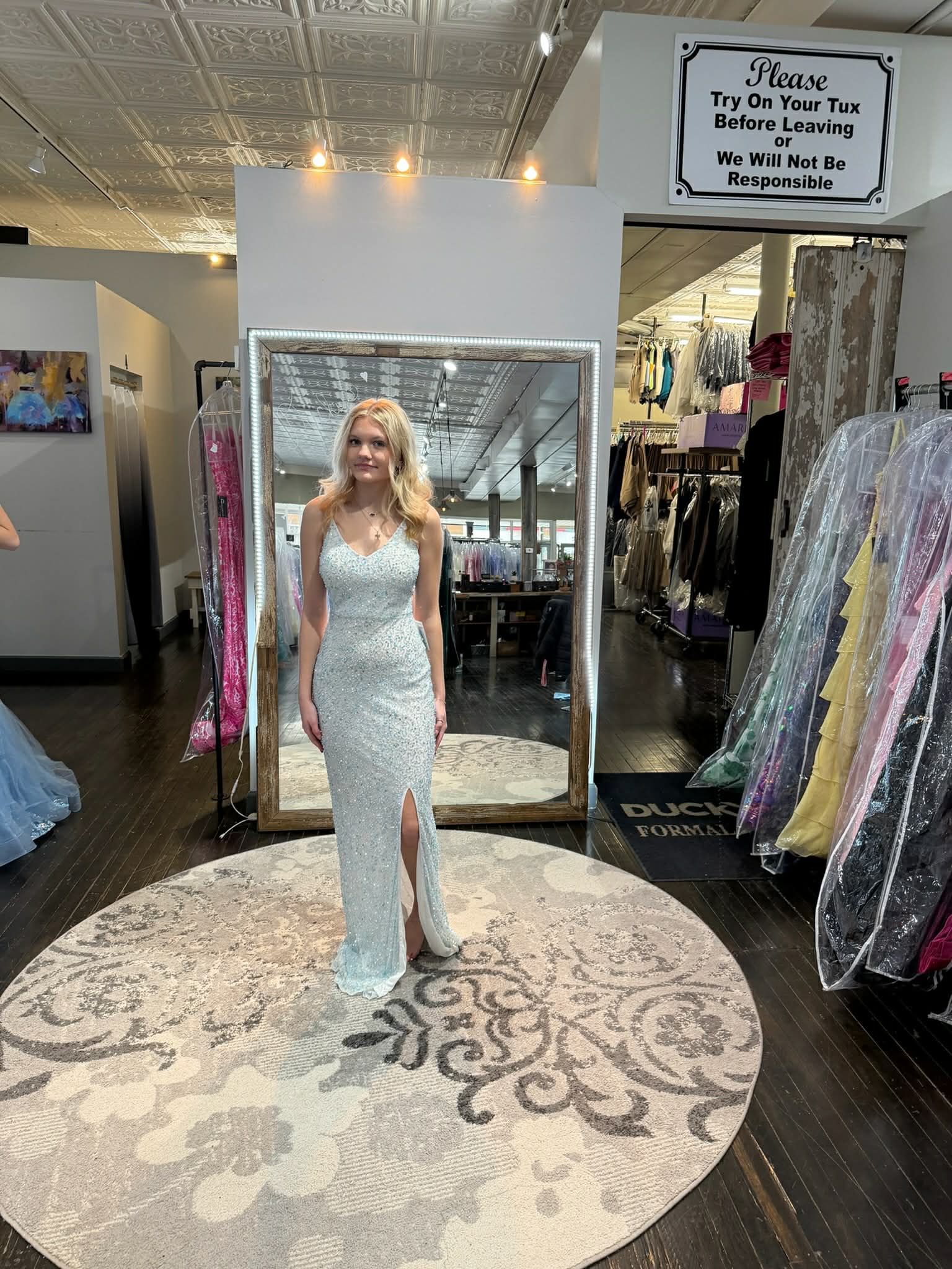 A person wearing a light blue, floor-length embellished evening gown with a thigh-high slit stands in a clothing store.