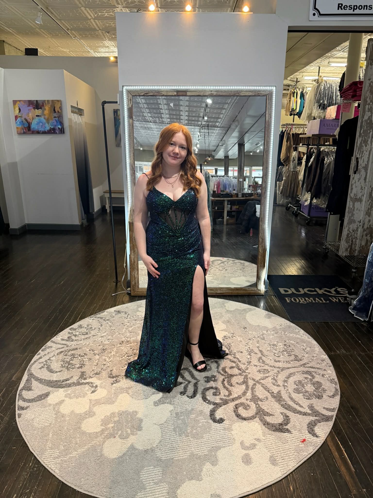 A person wearing a dark green sequined floor-length dress with a thigh-high slit, standing on a round rug in a store.