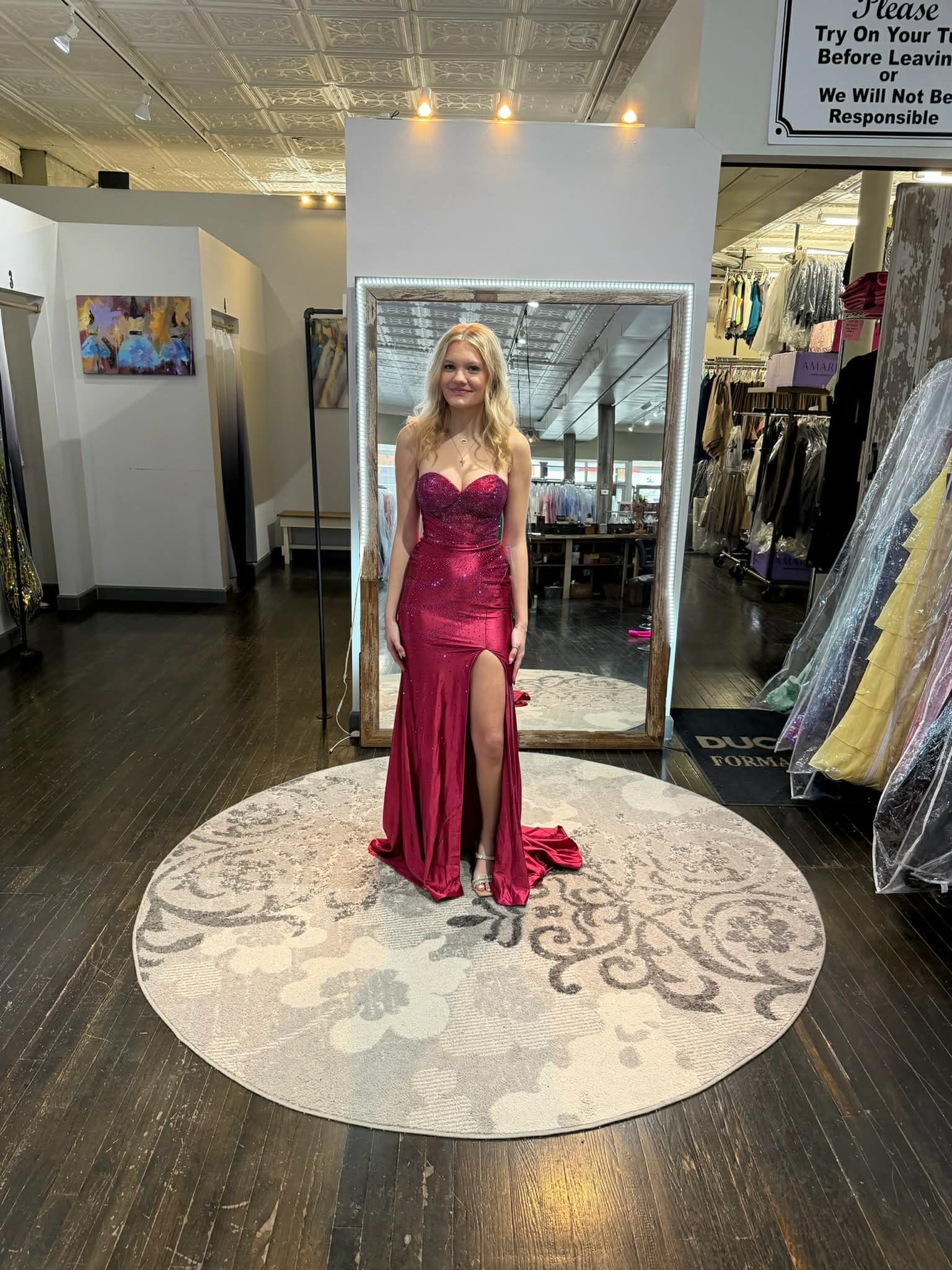 A person poses in a long, strapless, magenta gown with a thigh-high slit and intricate detailing in a clothing boutique.
