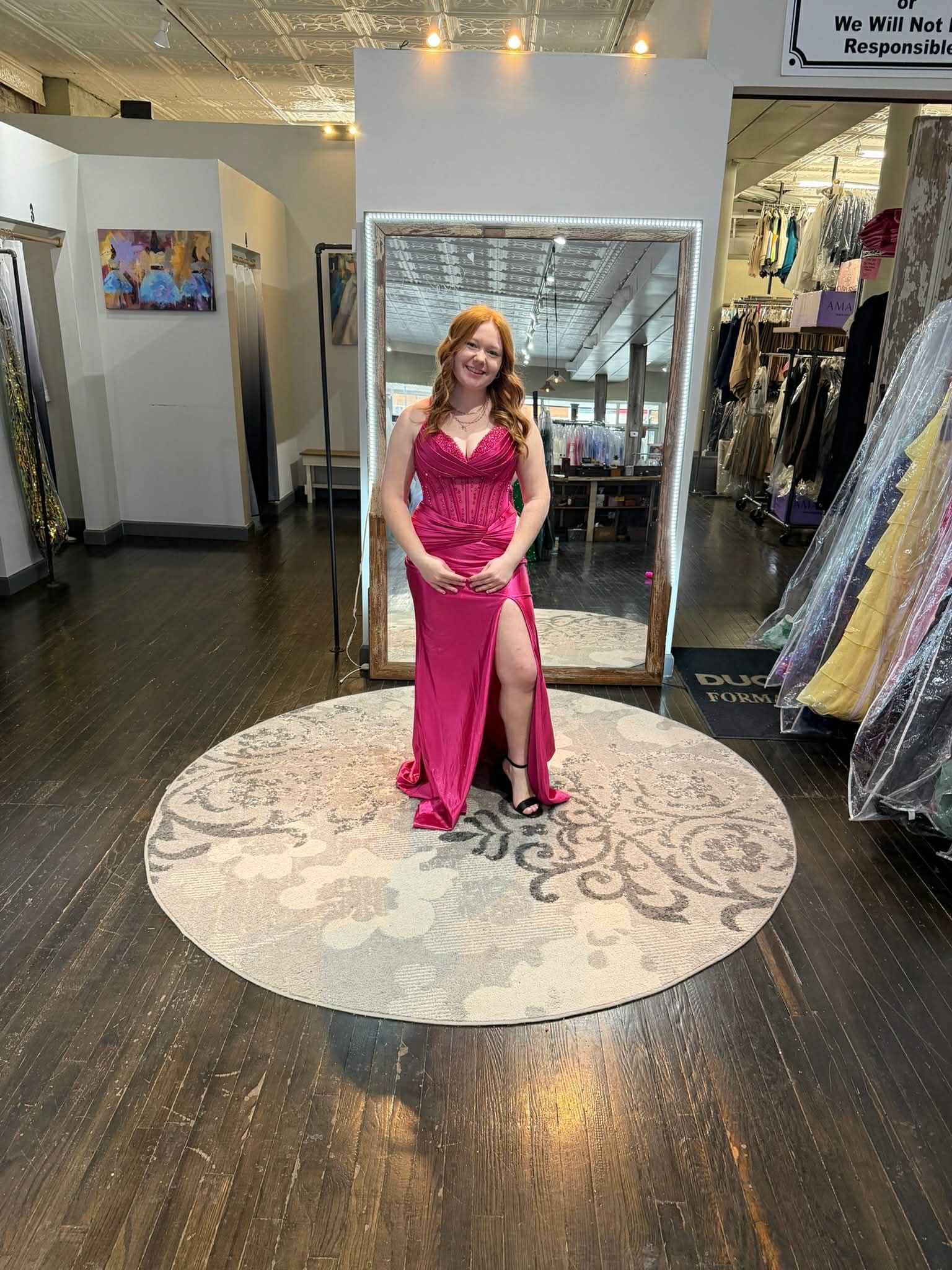 A person wearing a fuchsia floor-length gown with a high slit stands in a boutique on a circular patterned rug.