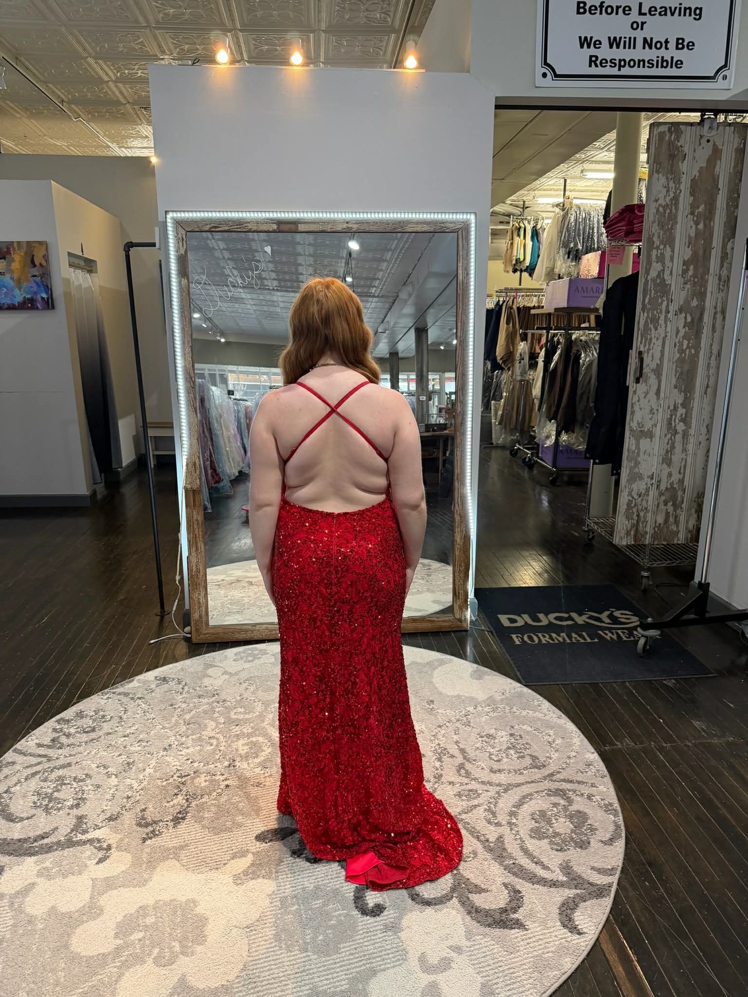 A person wearing a tiered, off-the-shoulder pink gown stands in a clothing store, reflected in a large dressing room mirror.