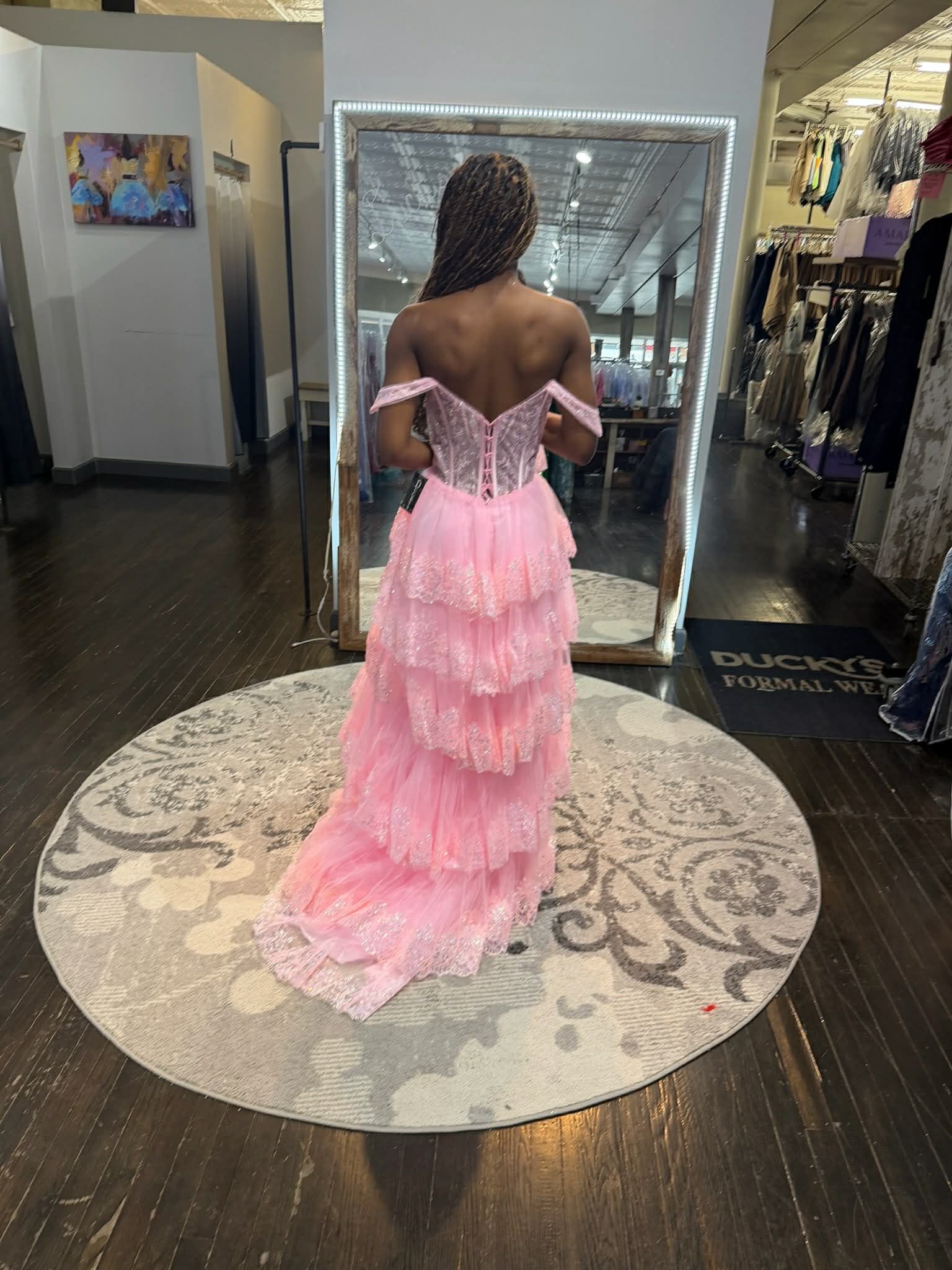 A person stands in a dress shop, modeling a floor-length, gold, sequined gown with a sheer bodice and a small train.