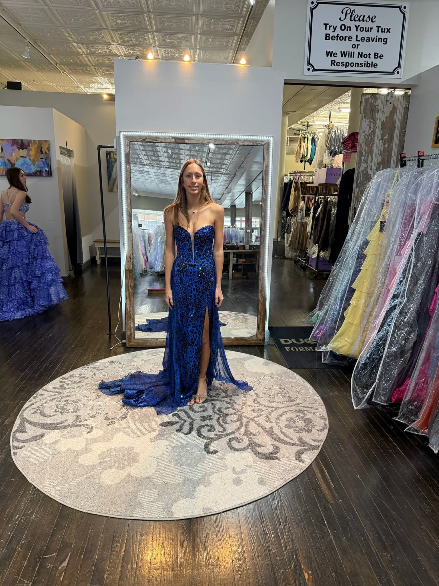 A person wearing a floor-length, beaded yellow gown stands in front of a mirror in a clothing store.