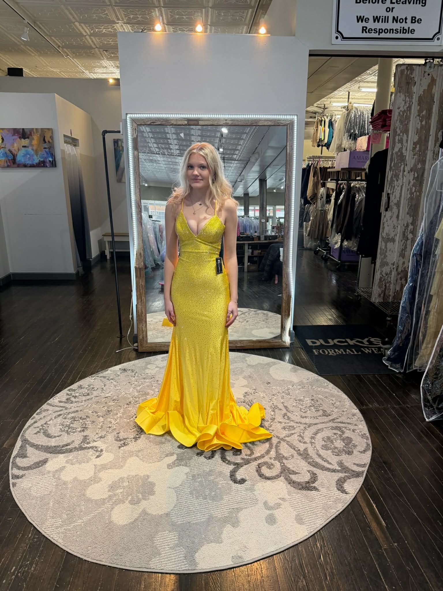 A person stands on a patterned rug, viewing their reflection in a large mirror while wearing a vibrant yellow sequined gown.