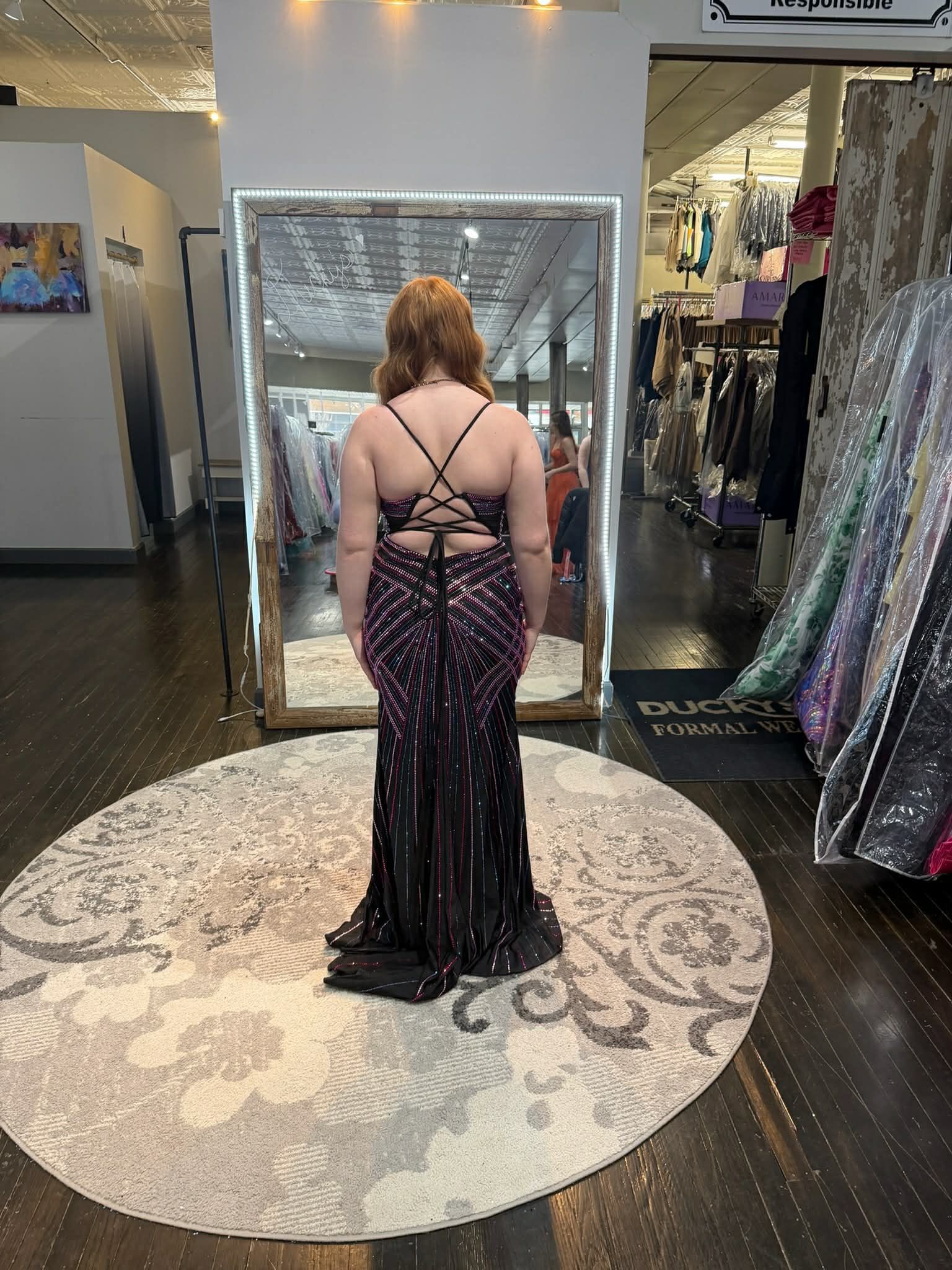 A person stands on a patterned rug in a clothing boutique, wearing a bright yellow, lace-up back floor-length gown.