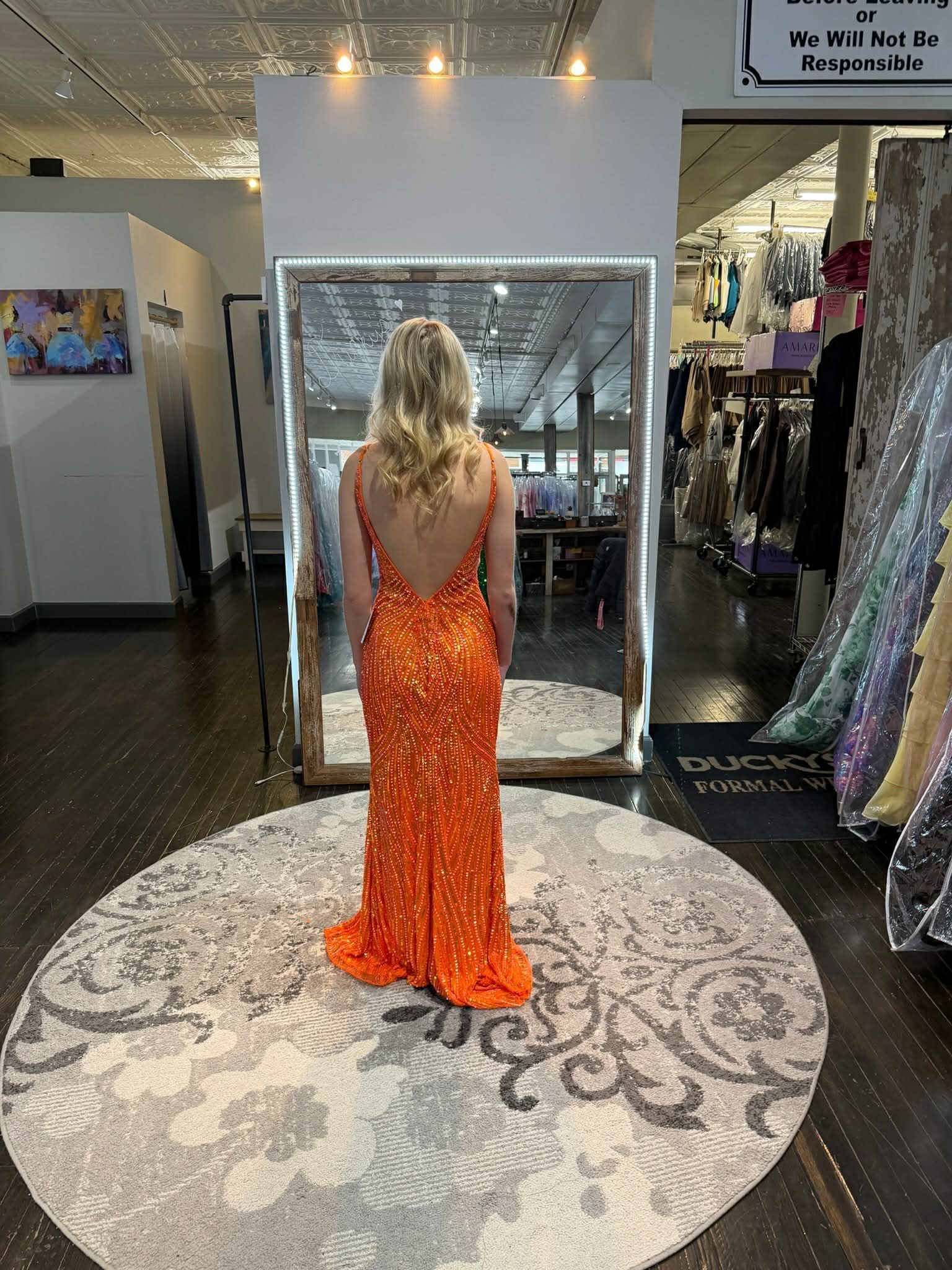 A person stands in a clothing store wearing a vibrant, fuchsia-colored, floor-length gown with ruffled accents.