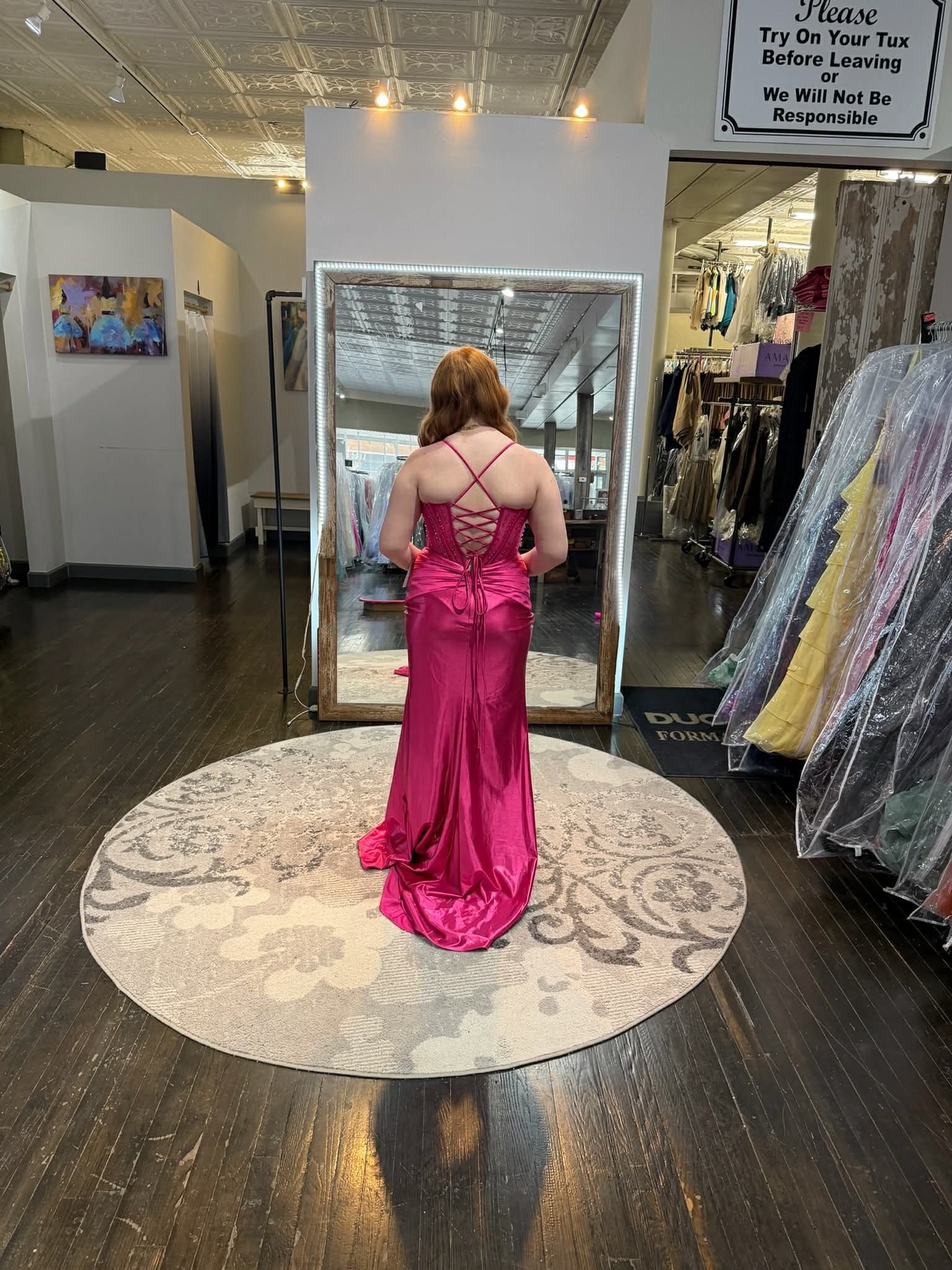 A person stands in a clothing store, facing a mirror while wearing a white, floor-length, embellished mermaid gown.