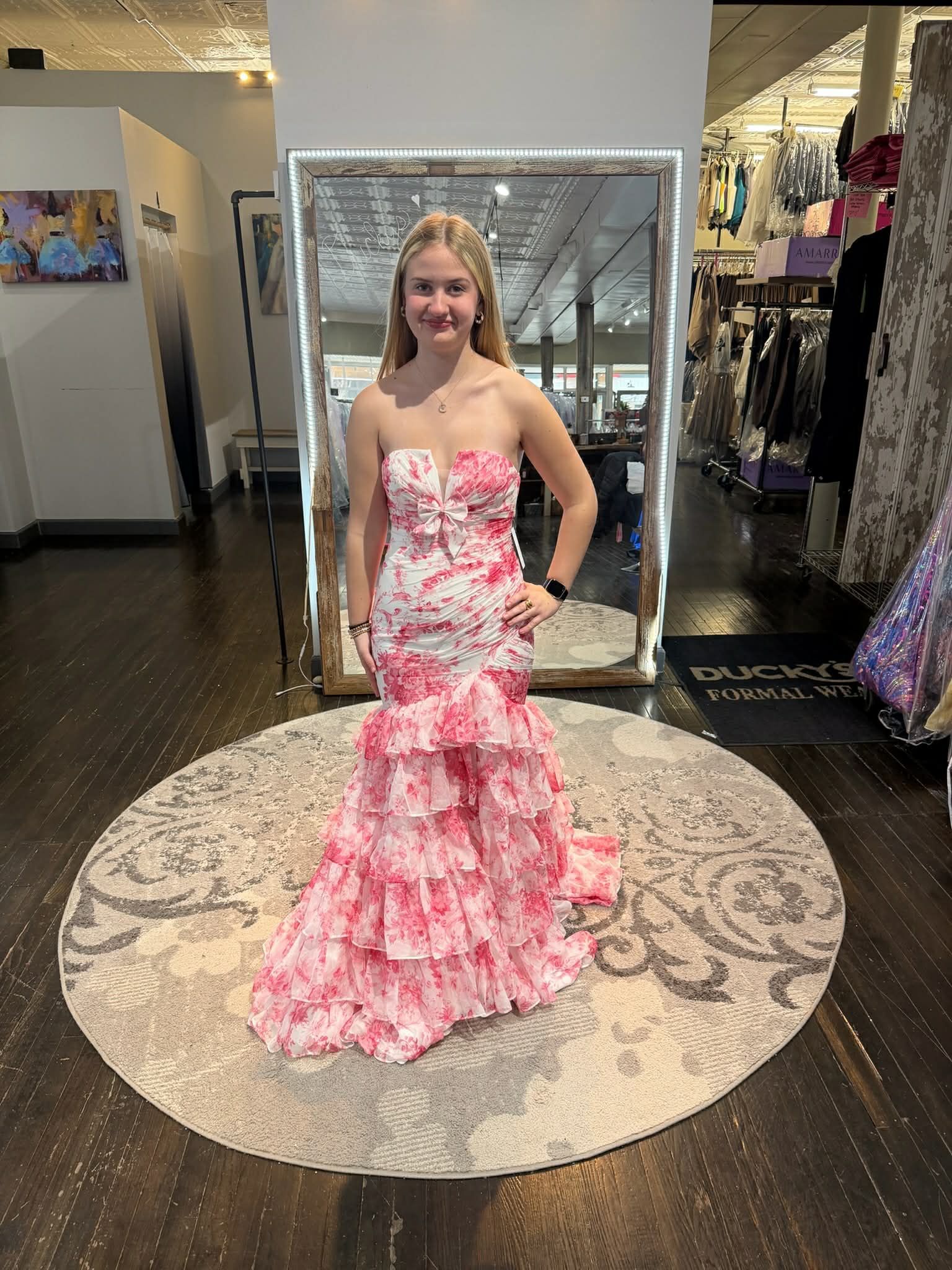 A person wearing a long, blue, floral-patterned dress with a cut-out back stands on a circular rug in a boutique.