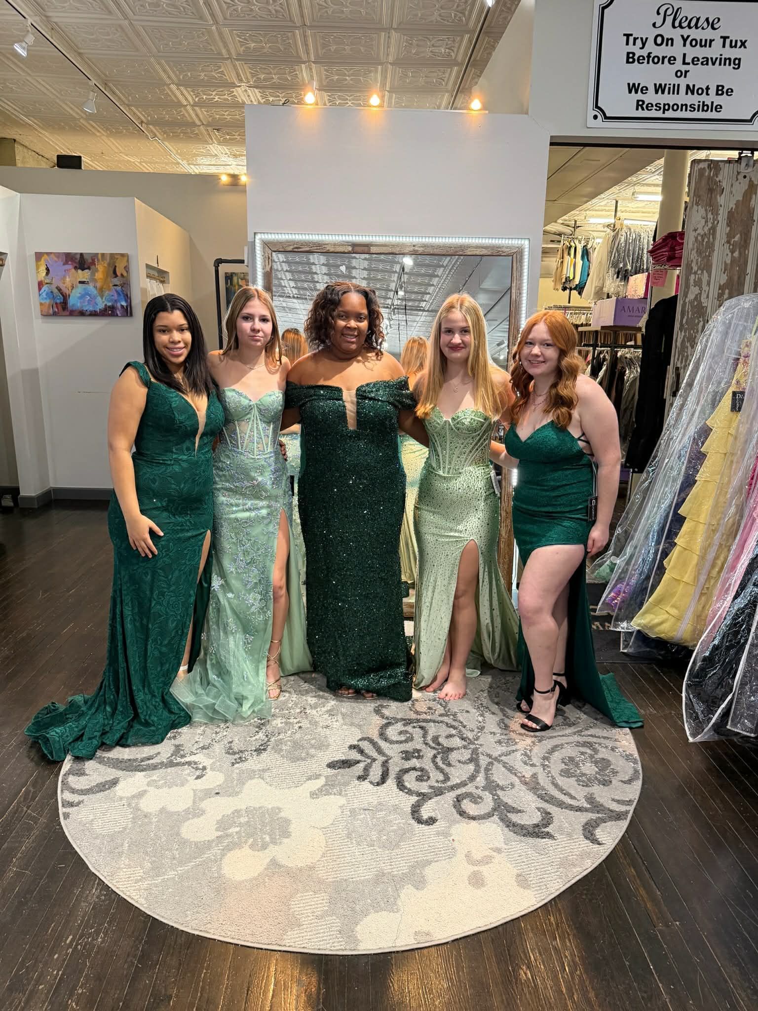 A person wearing a vibrant, fuchsia satin formal gown stands on a round rug in a clothing boutique, facing a large mirror.