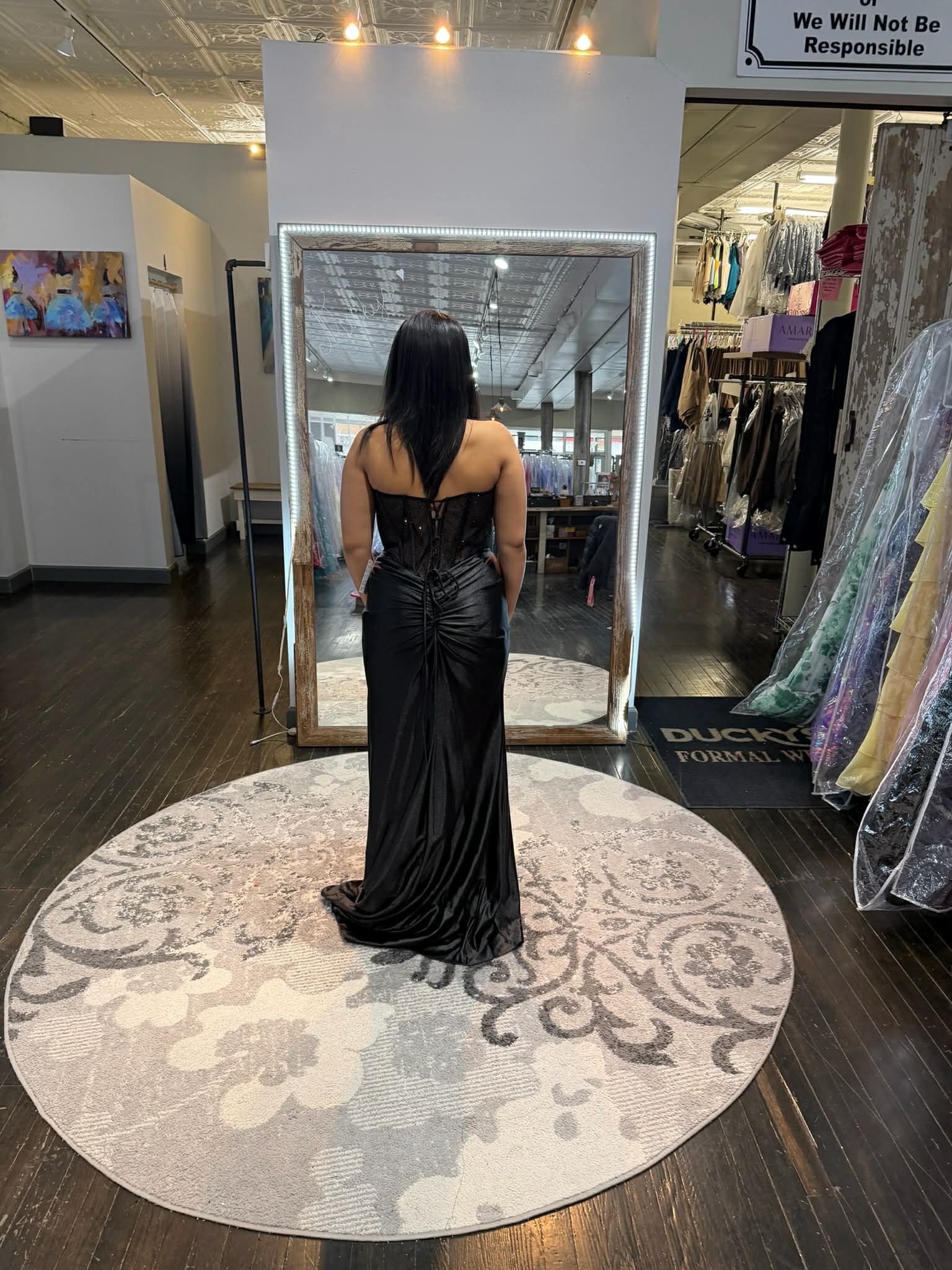 A person stands in a boutique, posing in a floor-length, silver sequined gown on a decorative circular rug.