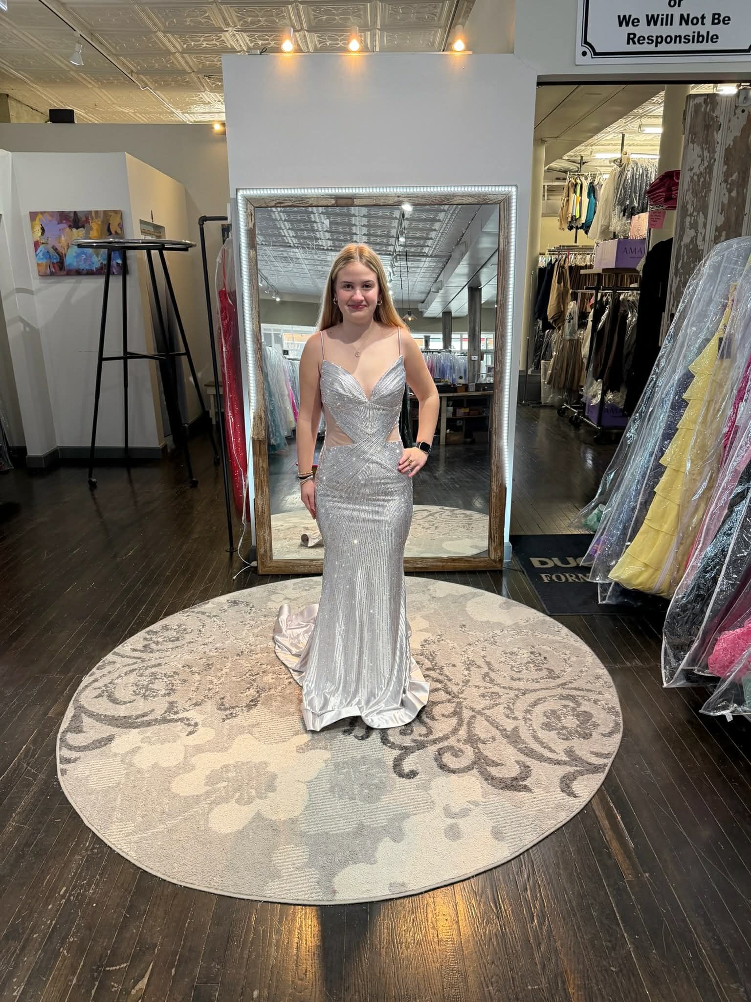 A person wearing a shimmering, gold, floor-length gown with a high slit, standing on a circular rug inside a boutique.