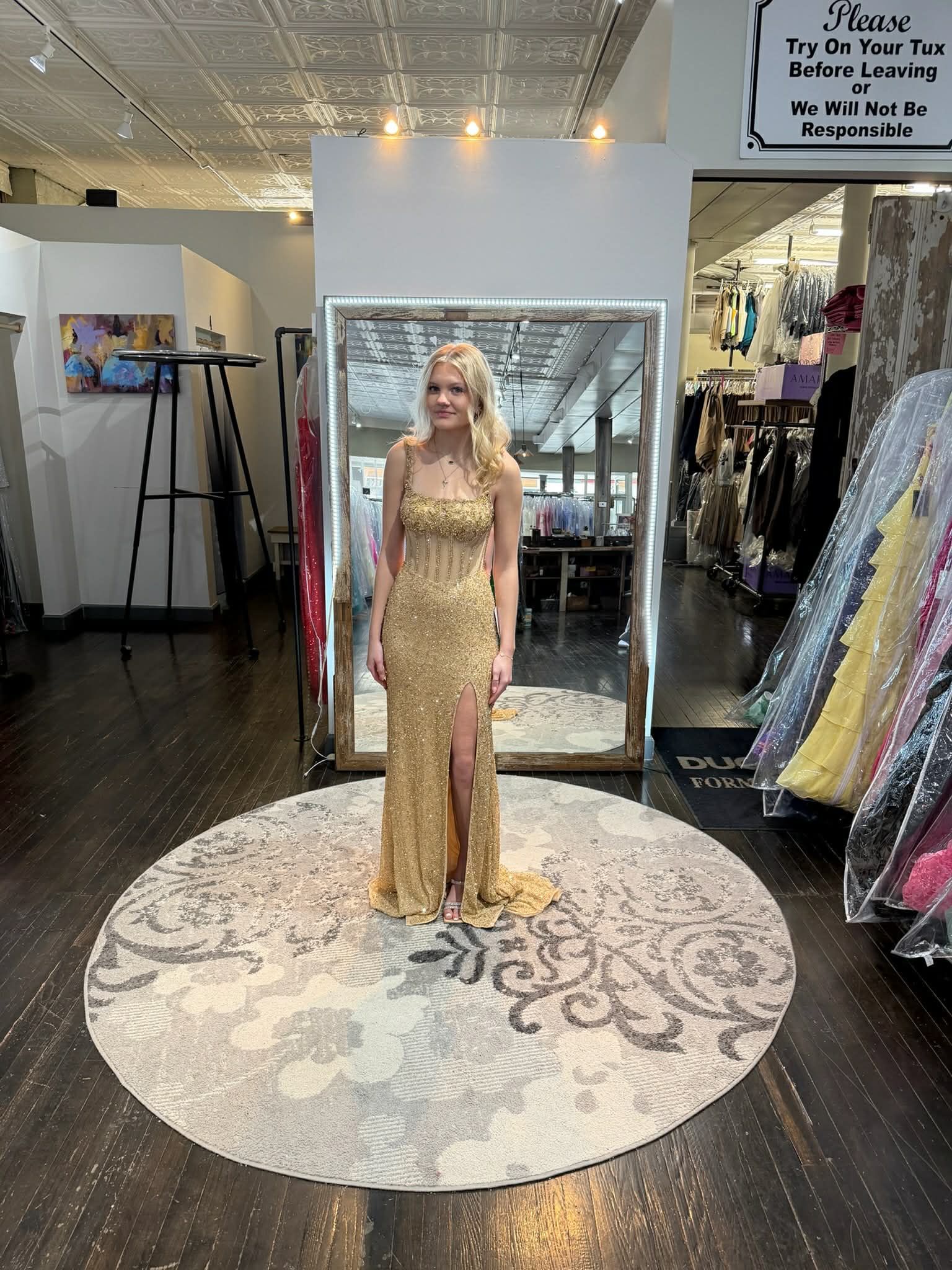 A person wears a strapless, bright yellow sequined dress with a ruffled high-low hem, standing on a rug in a dress shop.