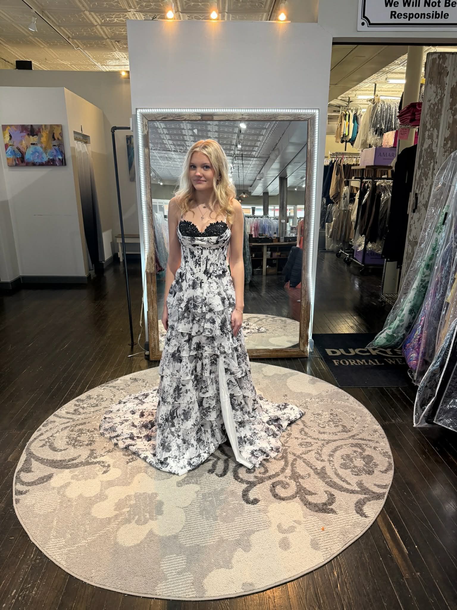 A person poses in a long, dark purple, beaded gown with a high slit, standing on a circular rug inside a clothing store.