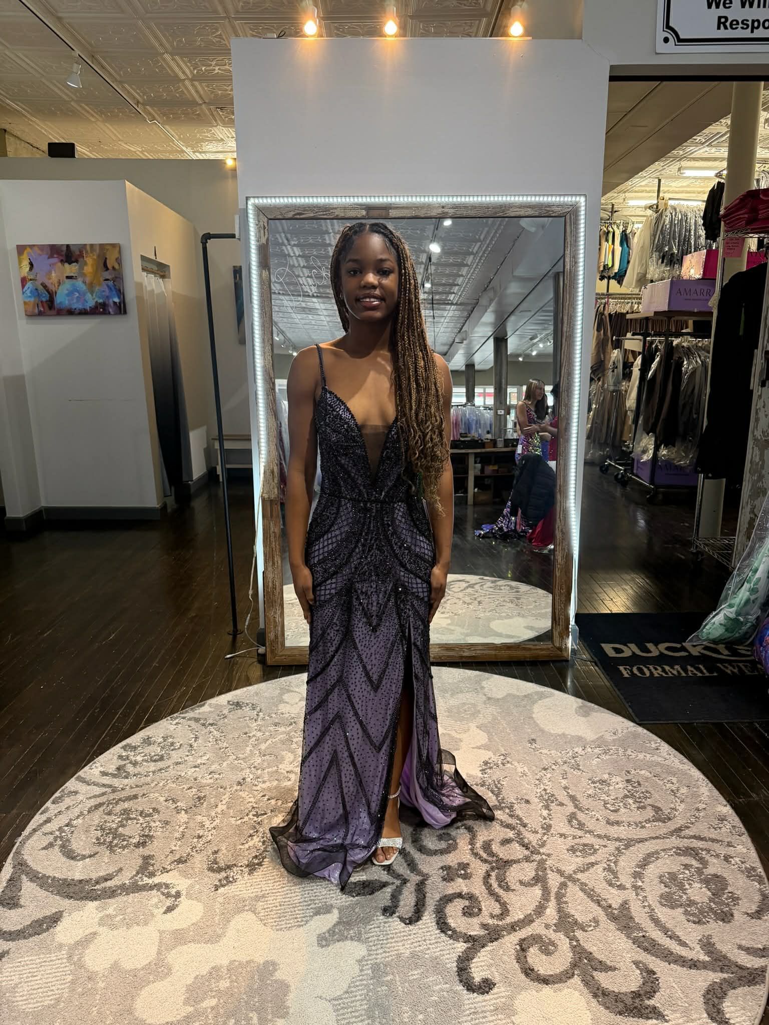 A person stands in a dress shop, facing a mirror, wearing a long, shimmering blue formal gown with a tiered train.