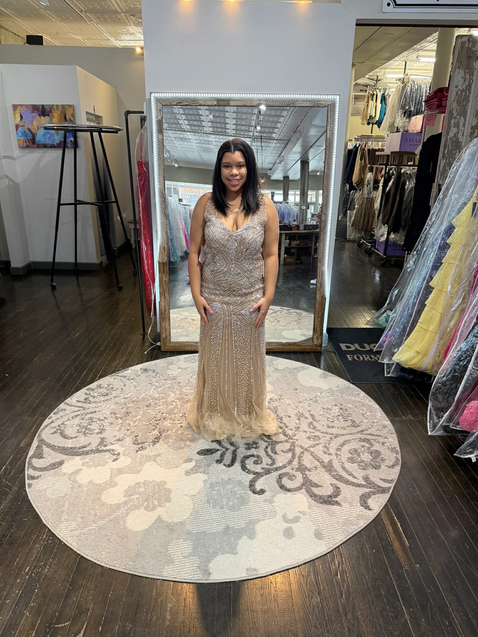A person in a store wearing a strapless, floor-length, pale blue satin mermaid-style gown standing before a large mirror.
