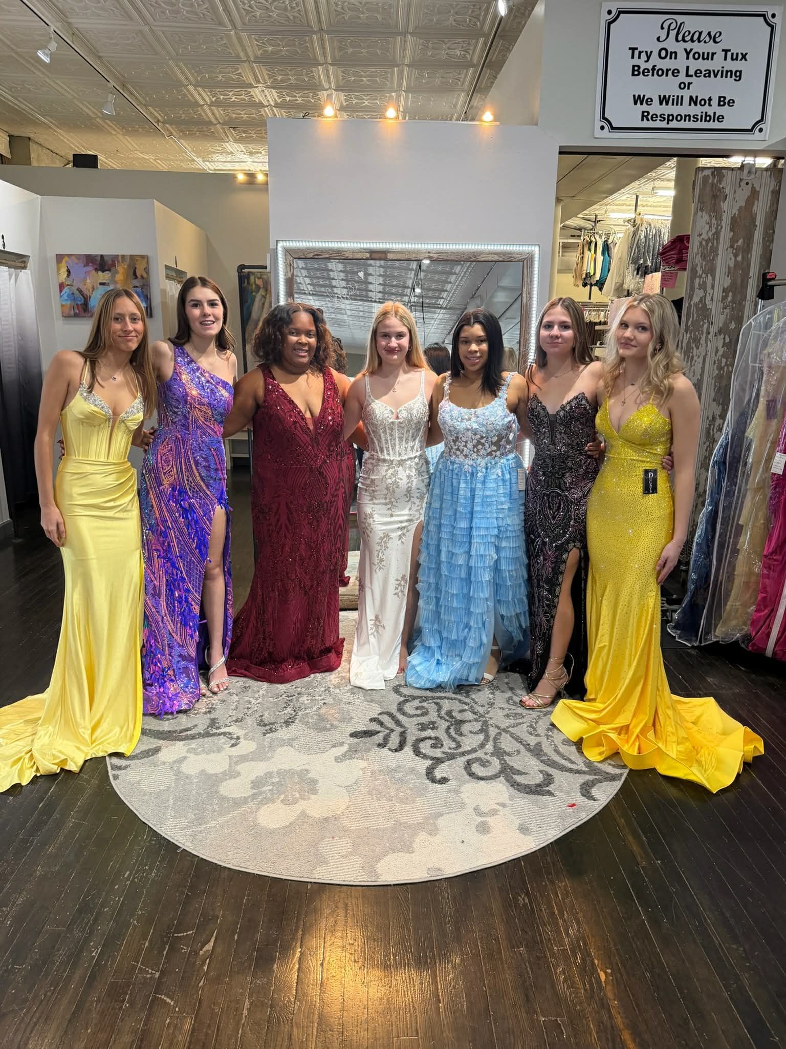 A person stands in a dress shop, facing a mirror while wearing a light green, floor-length, sequined mermaid-style gown.