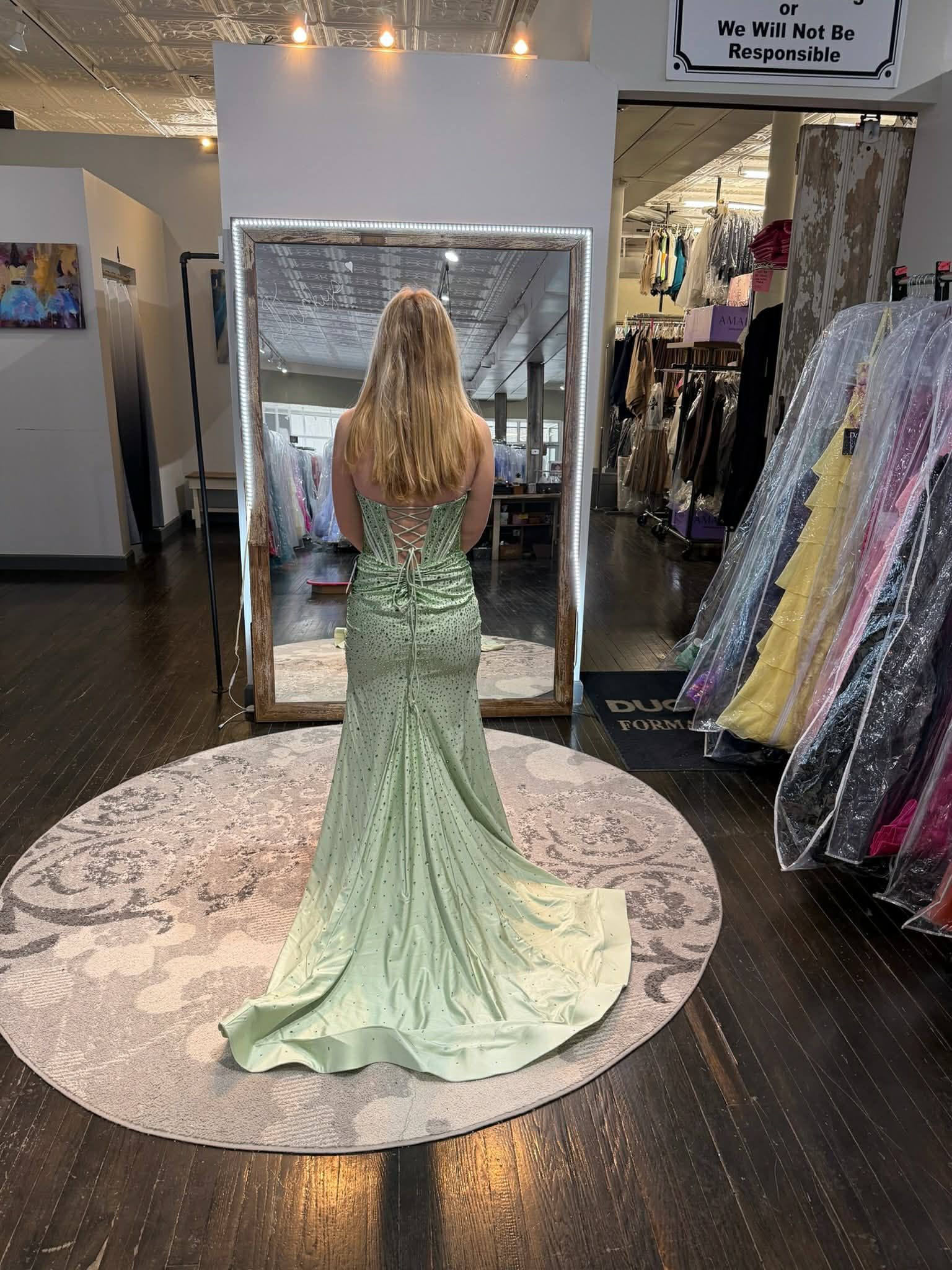 A person wearing a sparkling, floor-length red gown with a low back stands on a round rug in a clothing boutique.