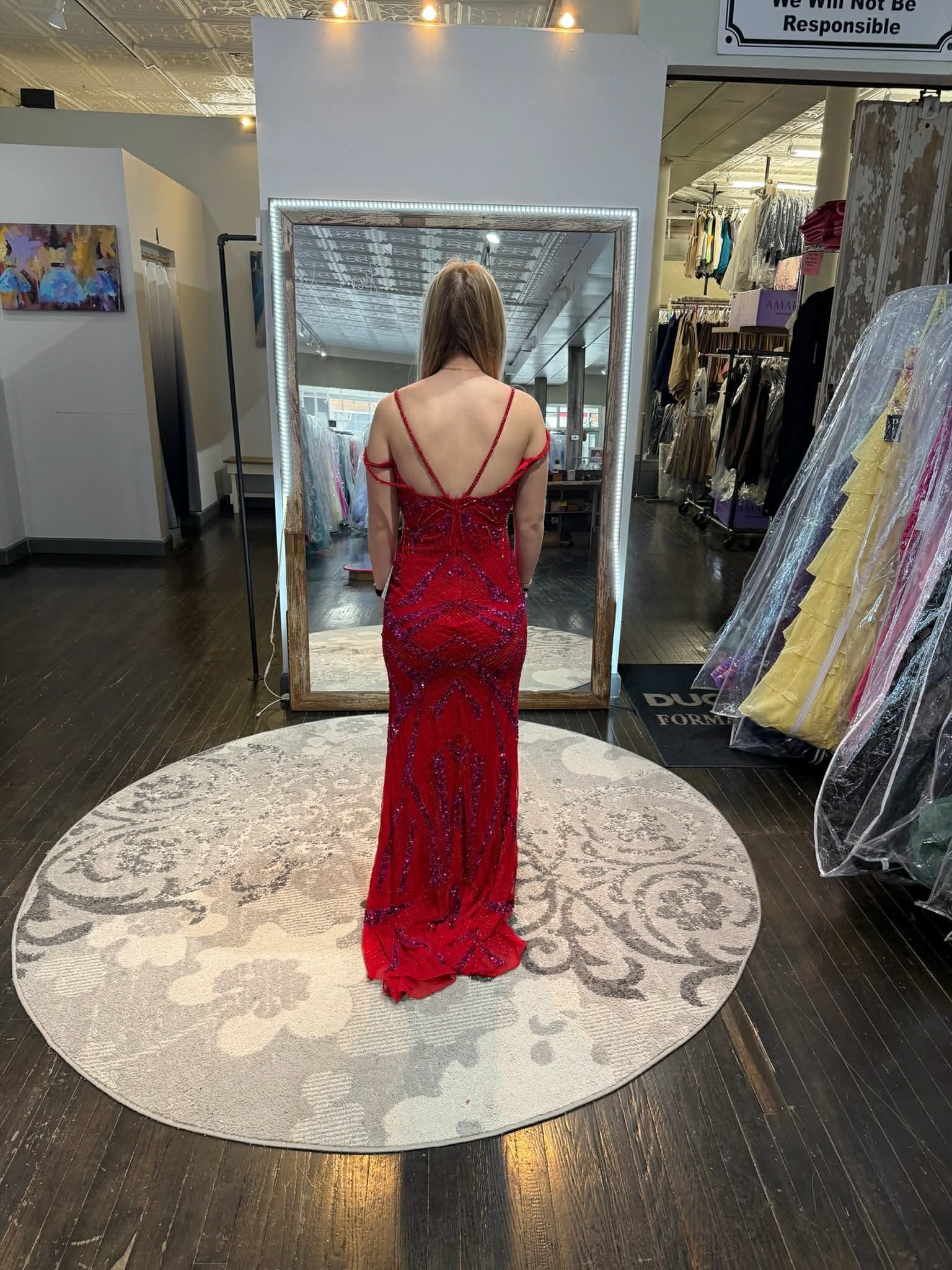 A person wearing a floor-length, orange, tiered tulle dress stands in front of a large mirror in a boutique.