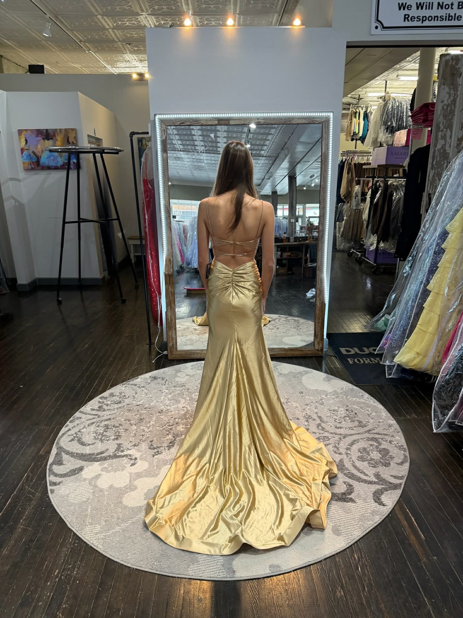 A person stands in a dress shop wearing a floor-length, dark sequined gown with a deep neckline and a thigh-high slit.