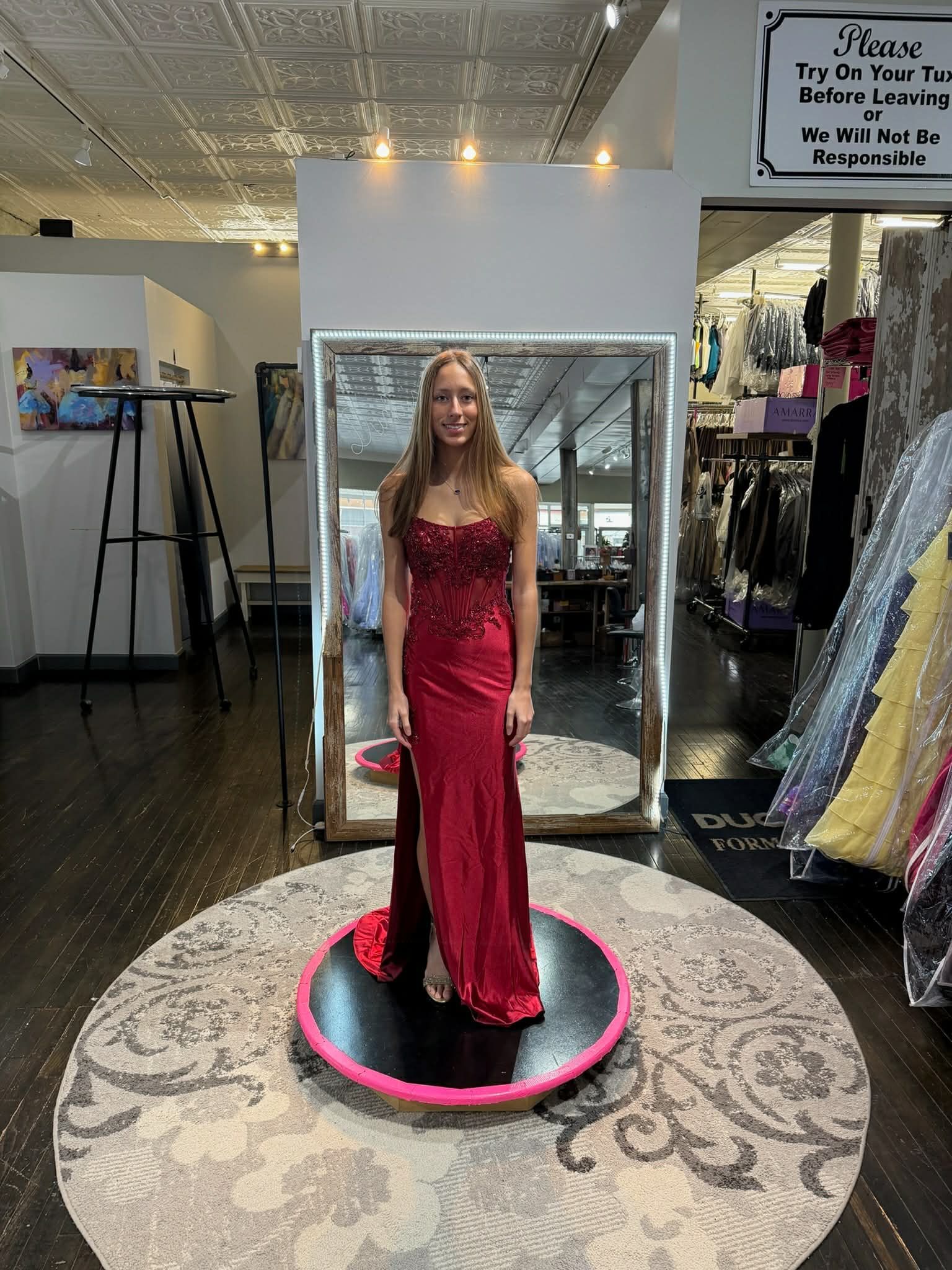 A person wearing a sparkling light blue, floor-length strapless gown stands on a round rug in a clothing boutique.
