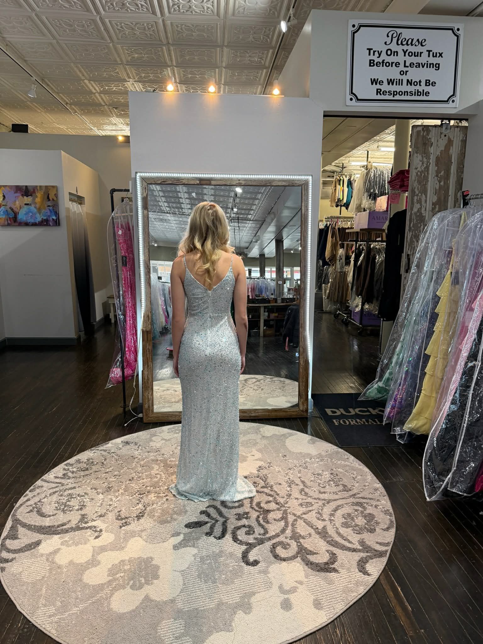 A person stands in a clothing store wearing a one-shoulder, cutout, sparkly red floor-length gown in front of a mirror.