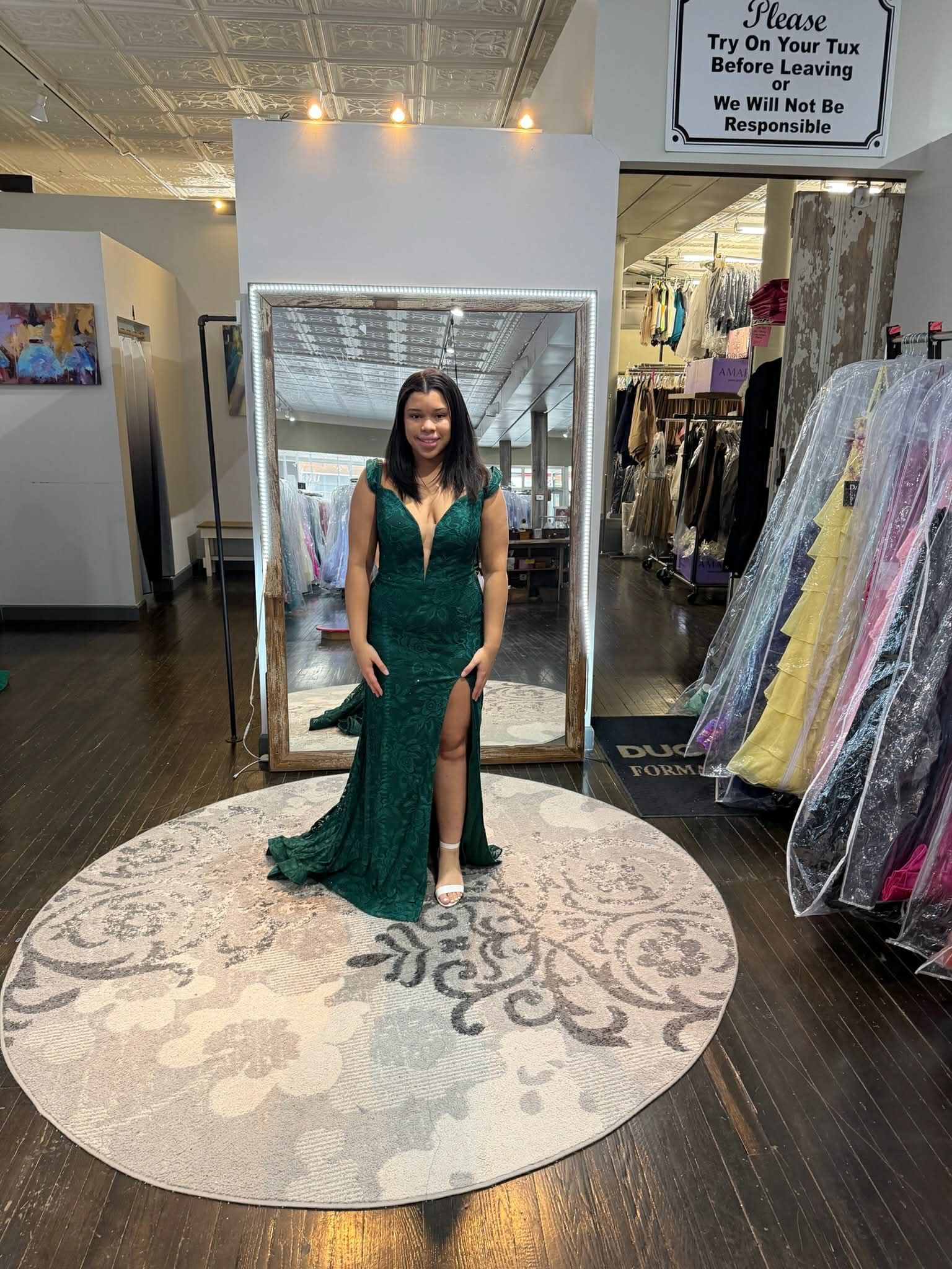 A person standing on a round rug in a clothing store, wearing a floor-length, red beaded gown viewed from behind.
