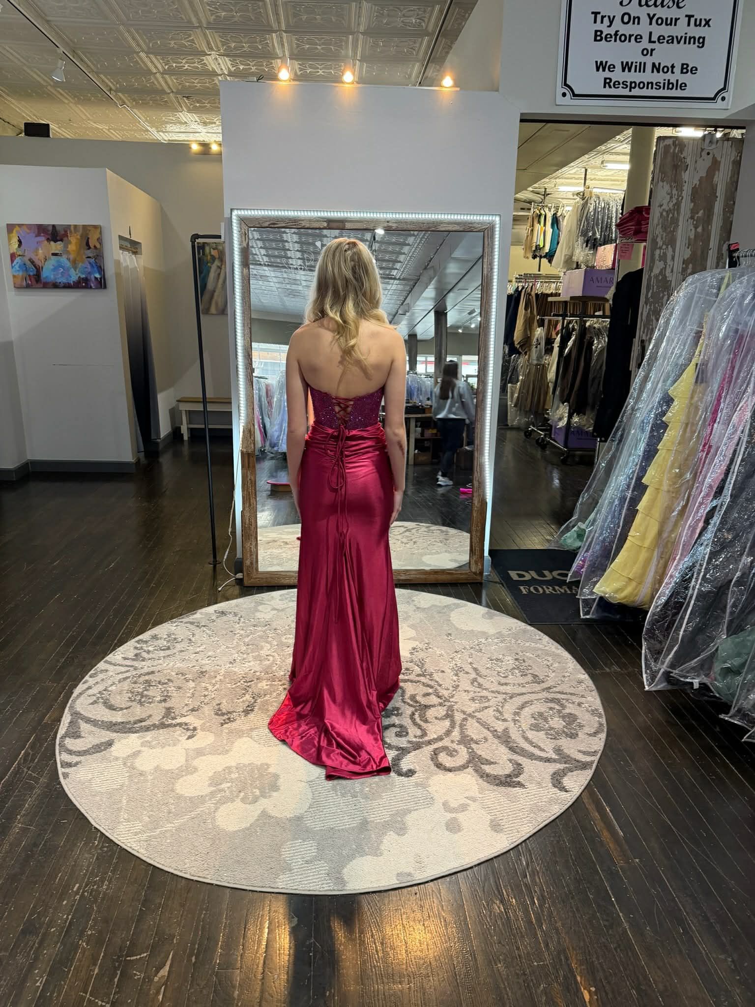 A person wearing a black floor-length formal dress with a corset bodice and side slit, standing in a clothing boutique.