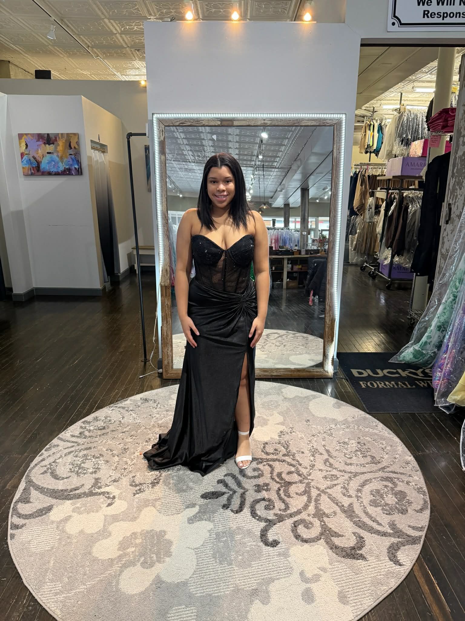 Nine people stand in a boutique, alternating between black and bright orange floor-length gowns in a line.