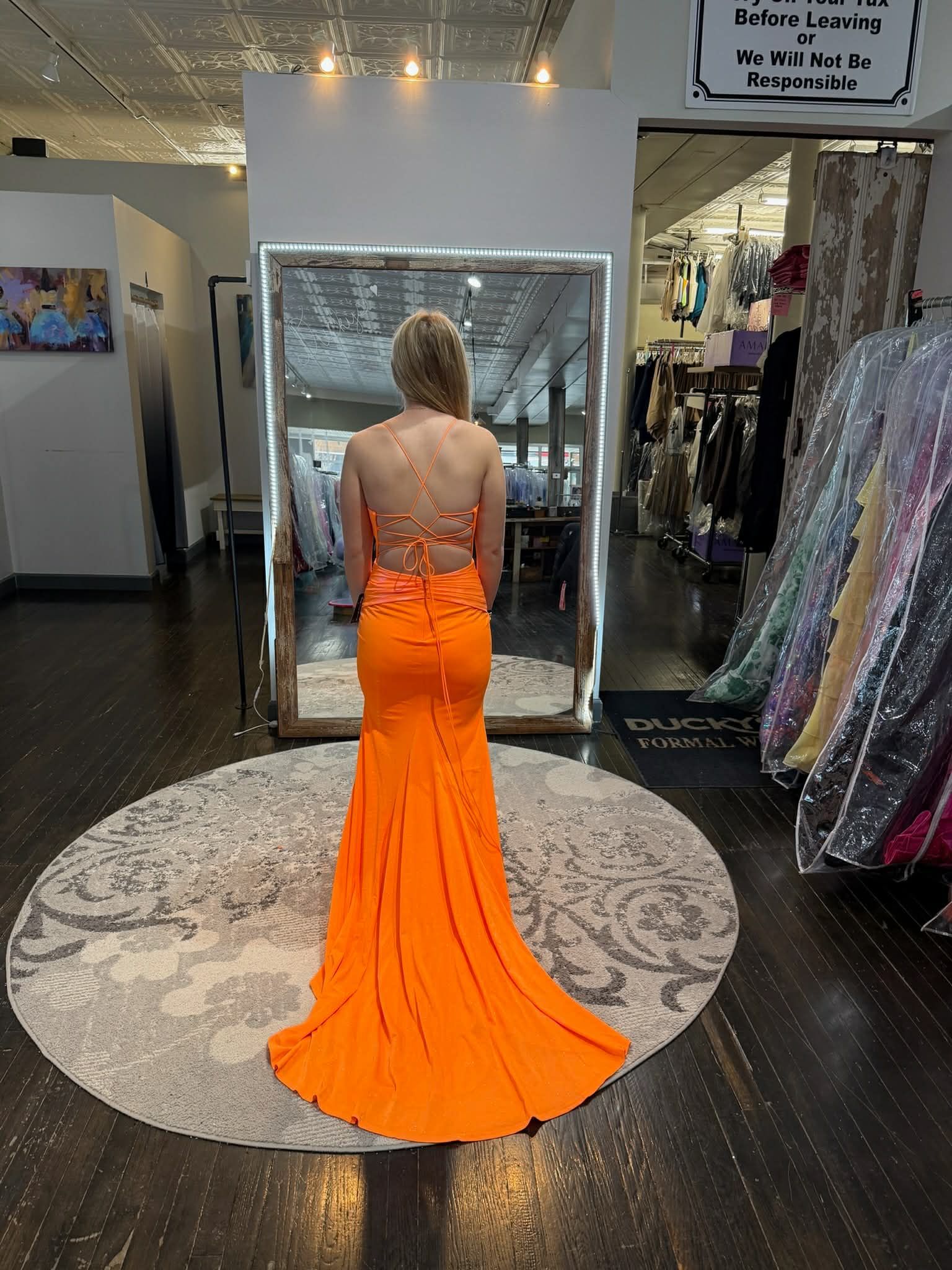 Nine people in colorful, floor-length formal gowns stand in a row inside a clothing boutique.