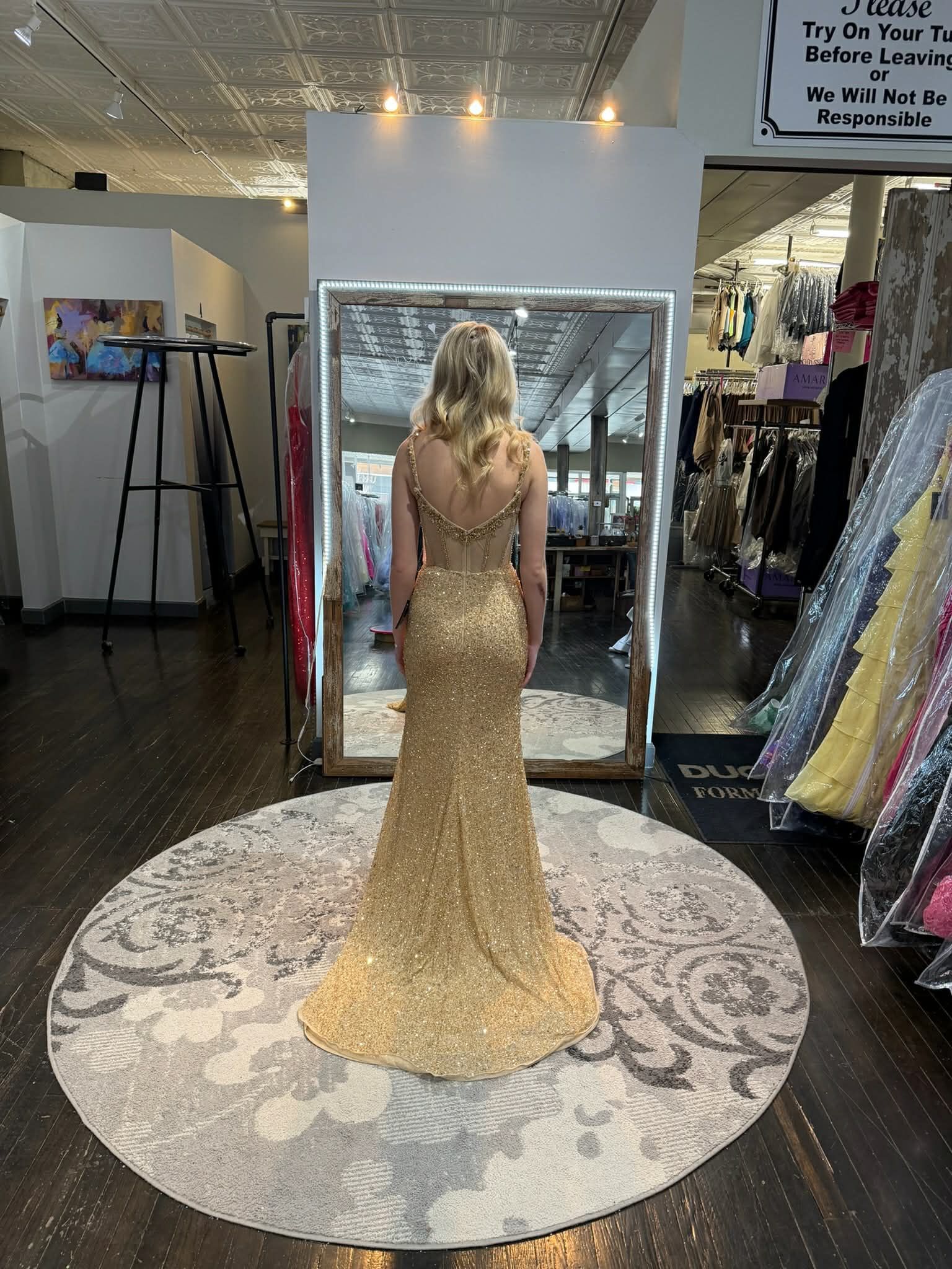 A person stands in a clothing store wearing a strapless, pink, tiered lace gown with an embellished corset bodice.