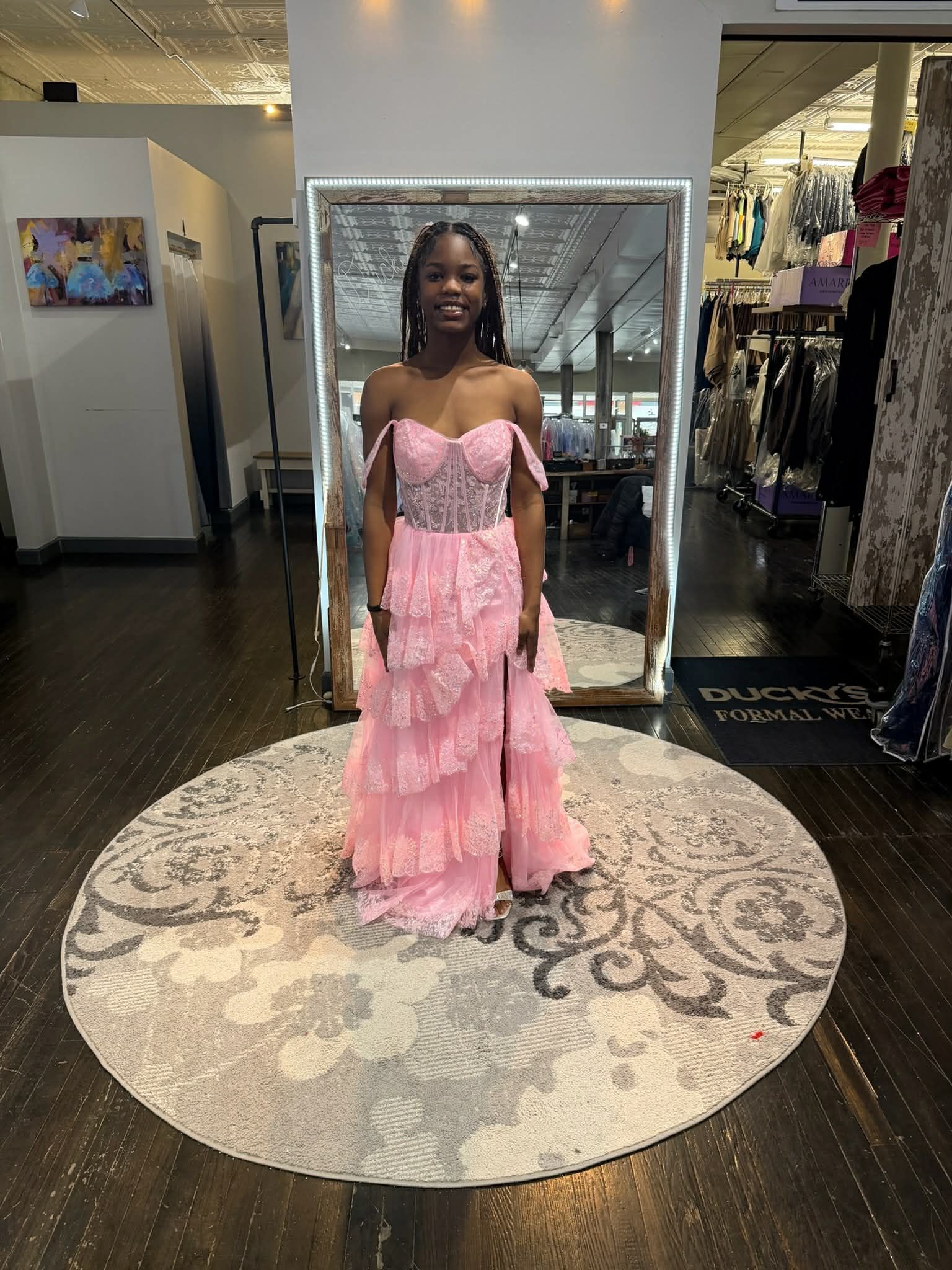 A person stands on a circular pedestal in a store, wearing a floor-length, backless, shiny red evening gown.