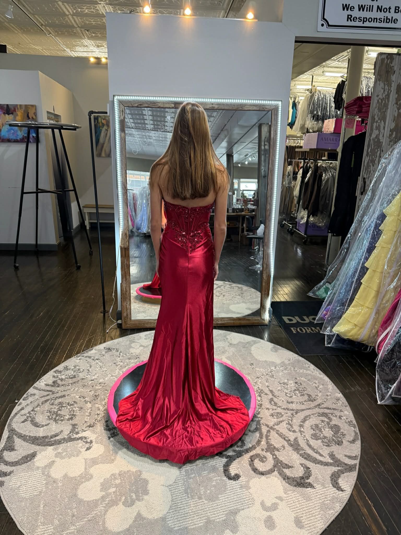 A person viewed from behind, wearing a floor-length, off-the-shoulder, black beaded evening gown in a clothing store.