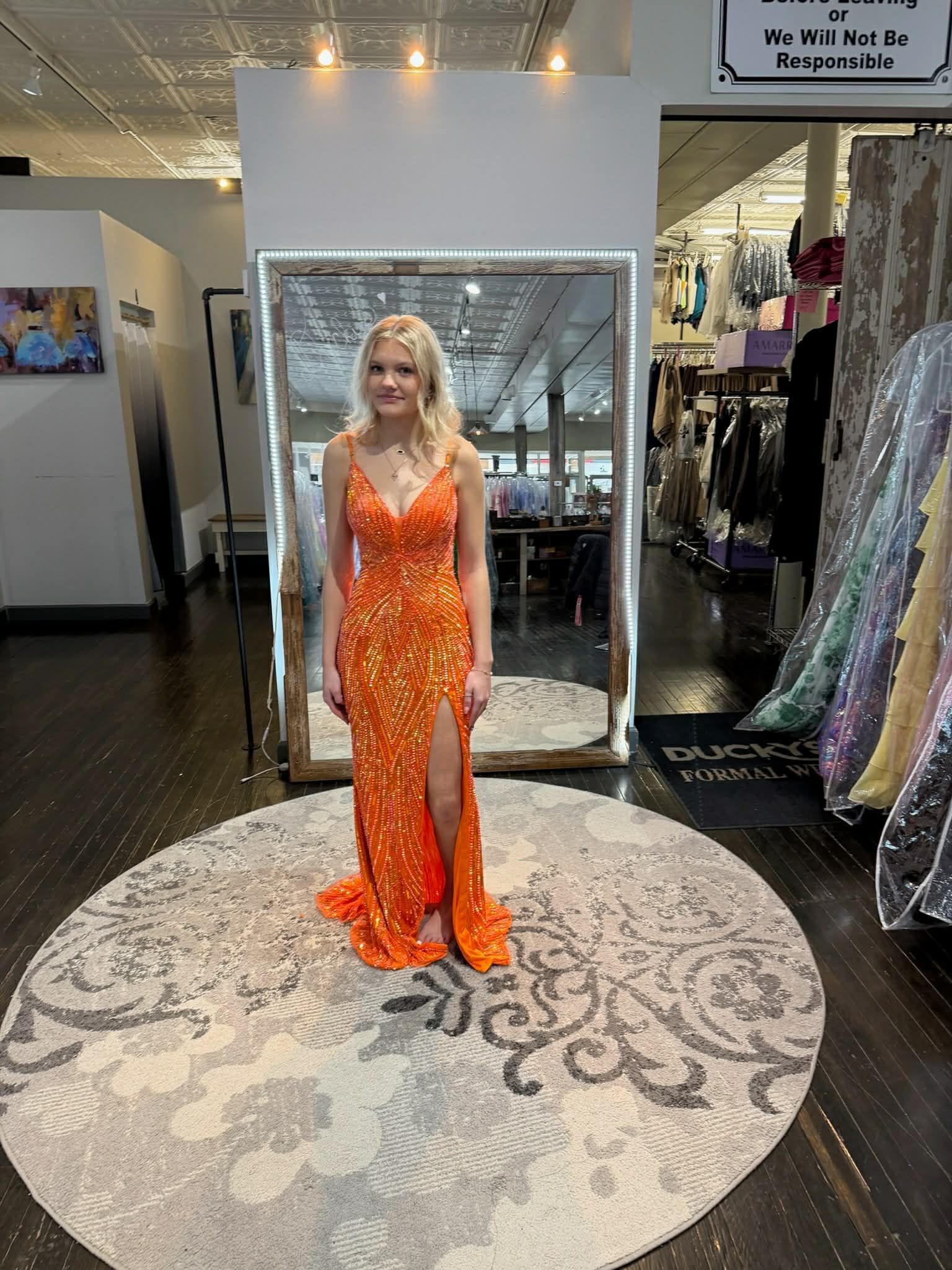 A person stands in a clothing store mirror wearing a floor-length, blue and white patterned evening gown with a slit.